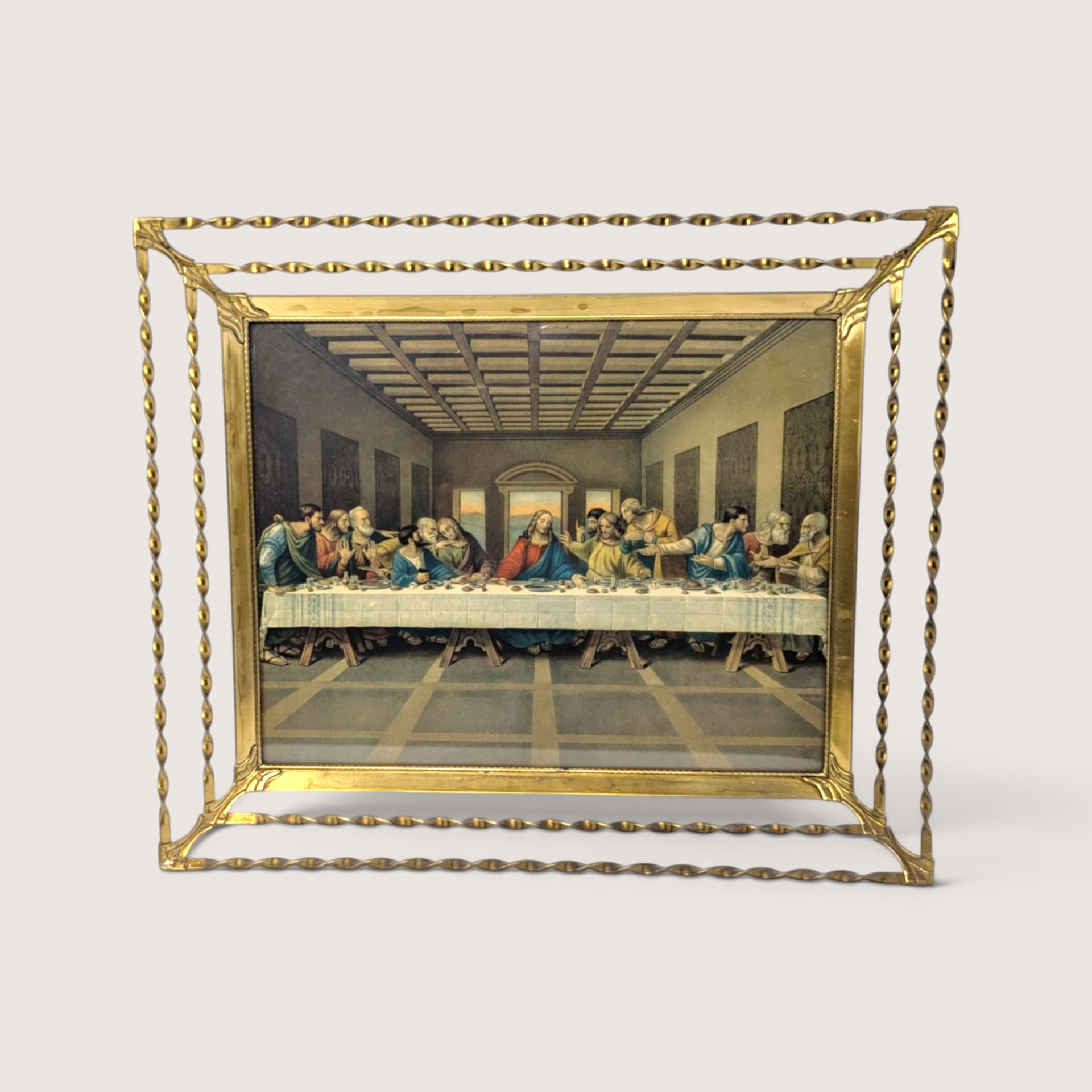A vintage Last Supper lithograph print housed in an ornate gold tone twisted metal wire frame on a cream background