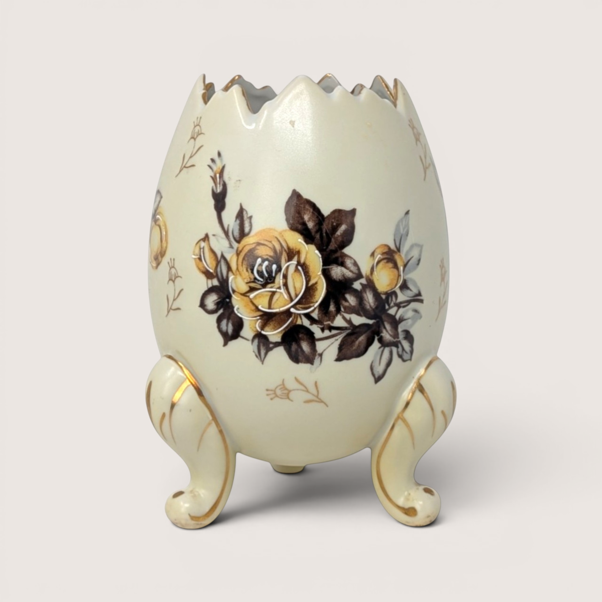 Cream colored footed egg vase with a cracked top edge and yellow rose design on a solid background.