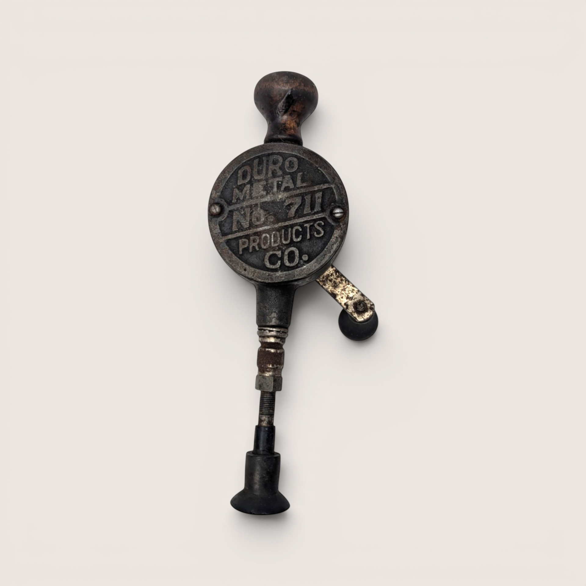 Antique metal hand crank valve lapping tool with a turned wood knob and suction cup base on a solid background.