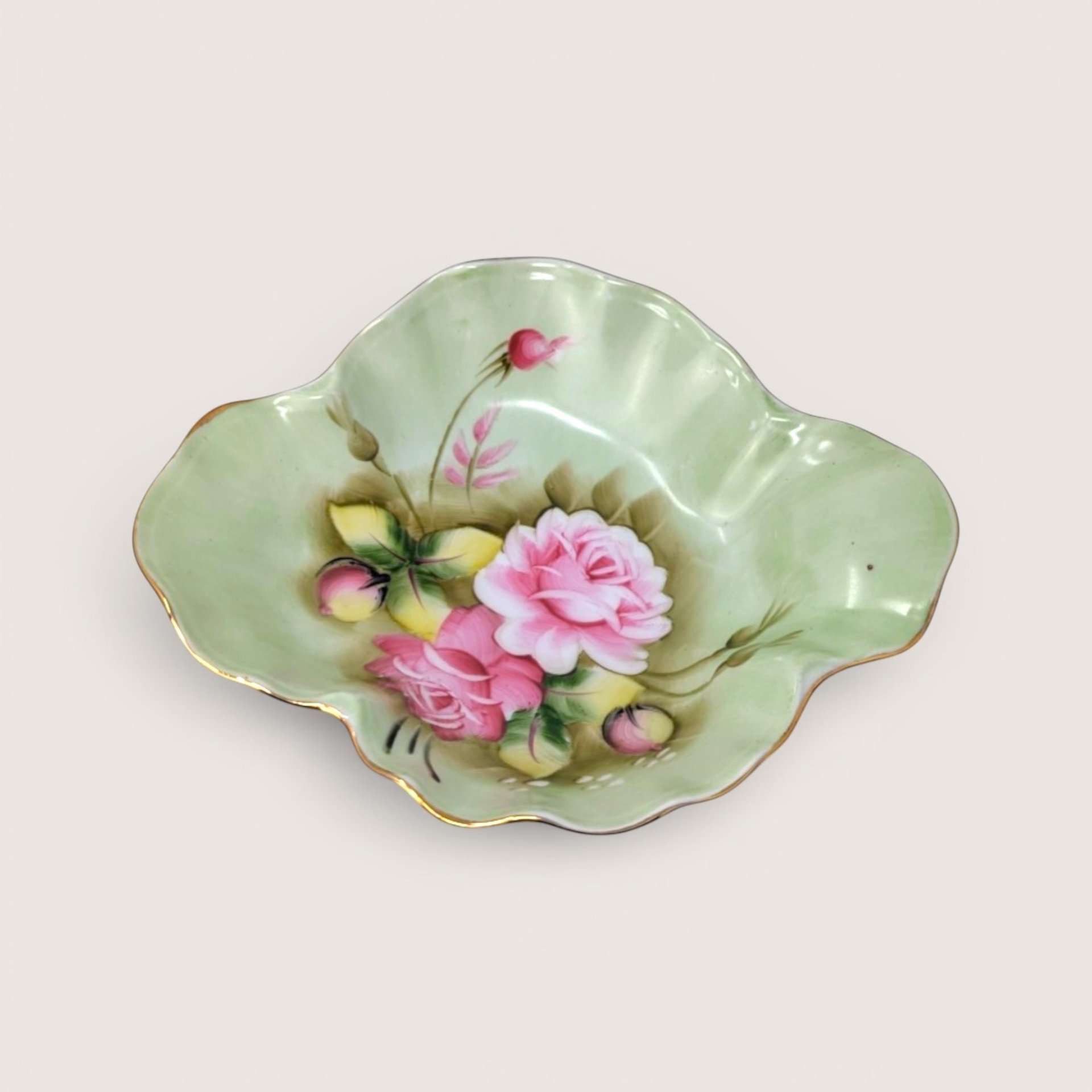 Fluted pale green porcelain candy dish with hand painted pink roses and gold gilt edges on a solid background.
