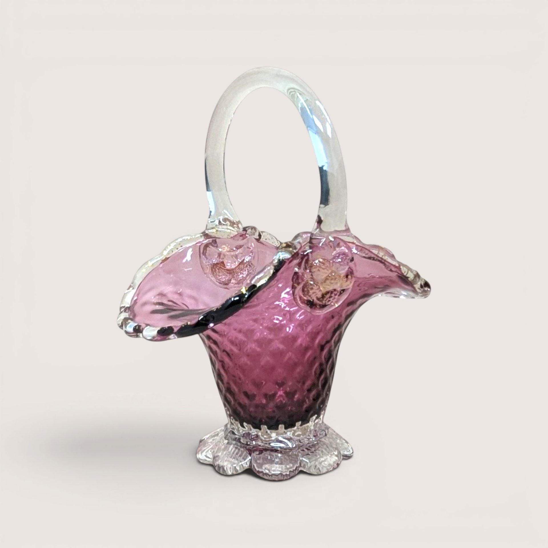 Cranberry pink glass basket with a textured diamond pattern ruffled silver crest rim and clear handle on a solid background.