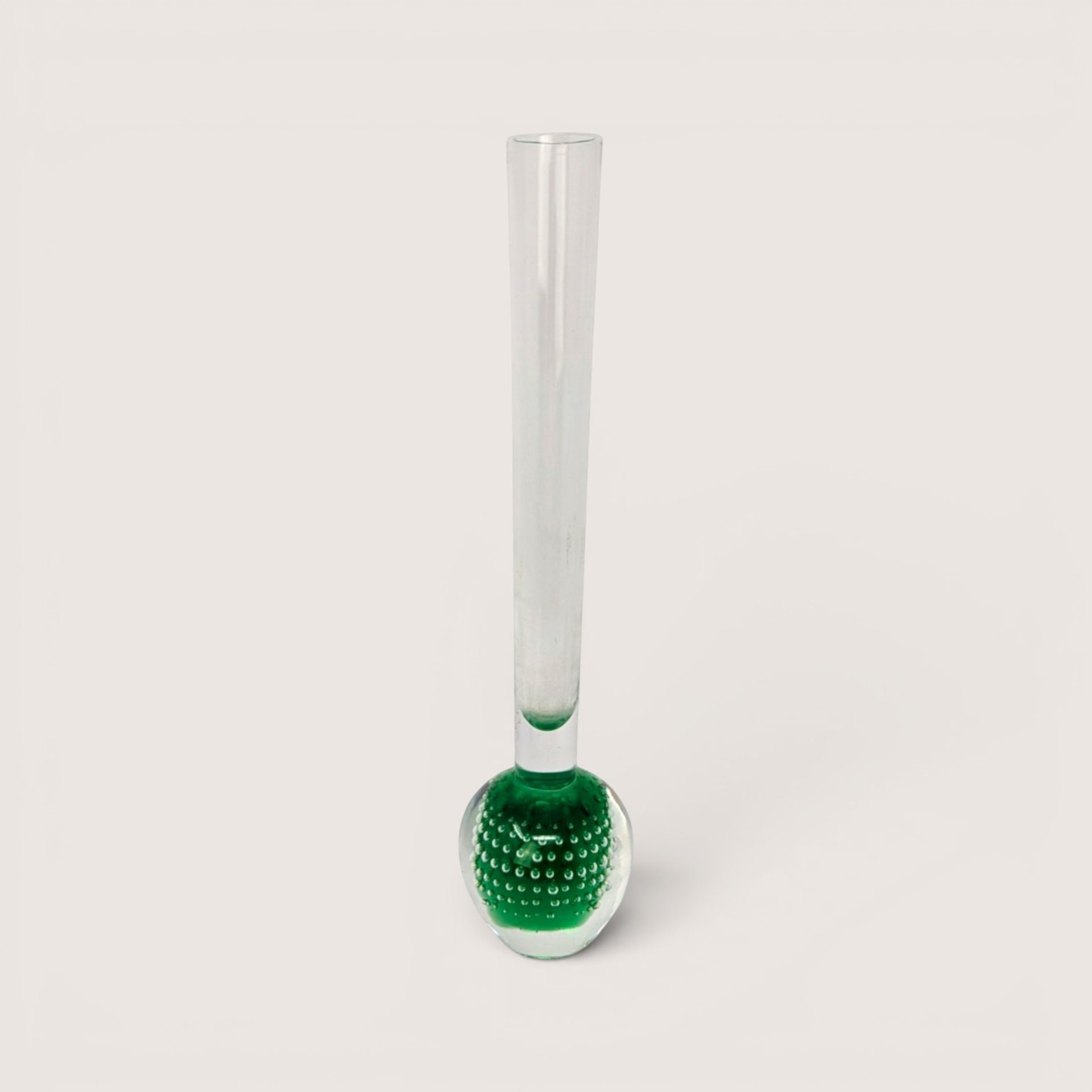 Slender clear glass bud vase with a heavy green bulbous base containing a controlled bubble pattern on a solid background.