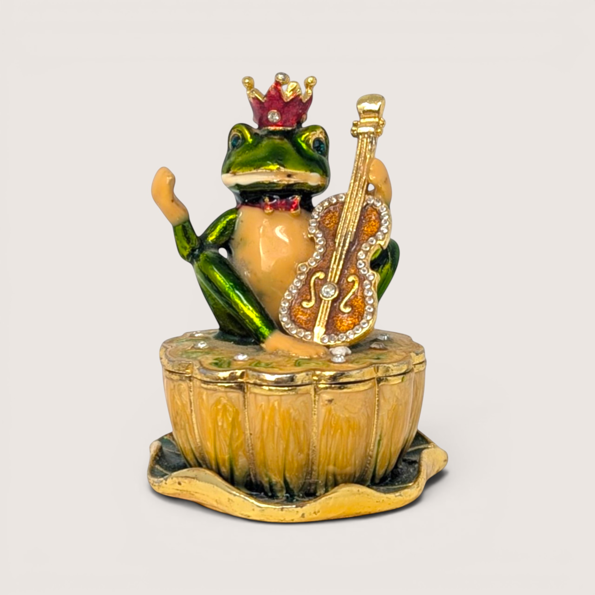 Enameled frog prince figurine wearing a crown and holding a violin atop a round pedestal trinket box.