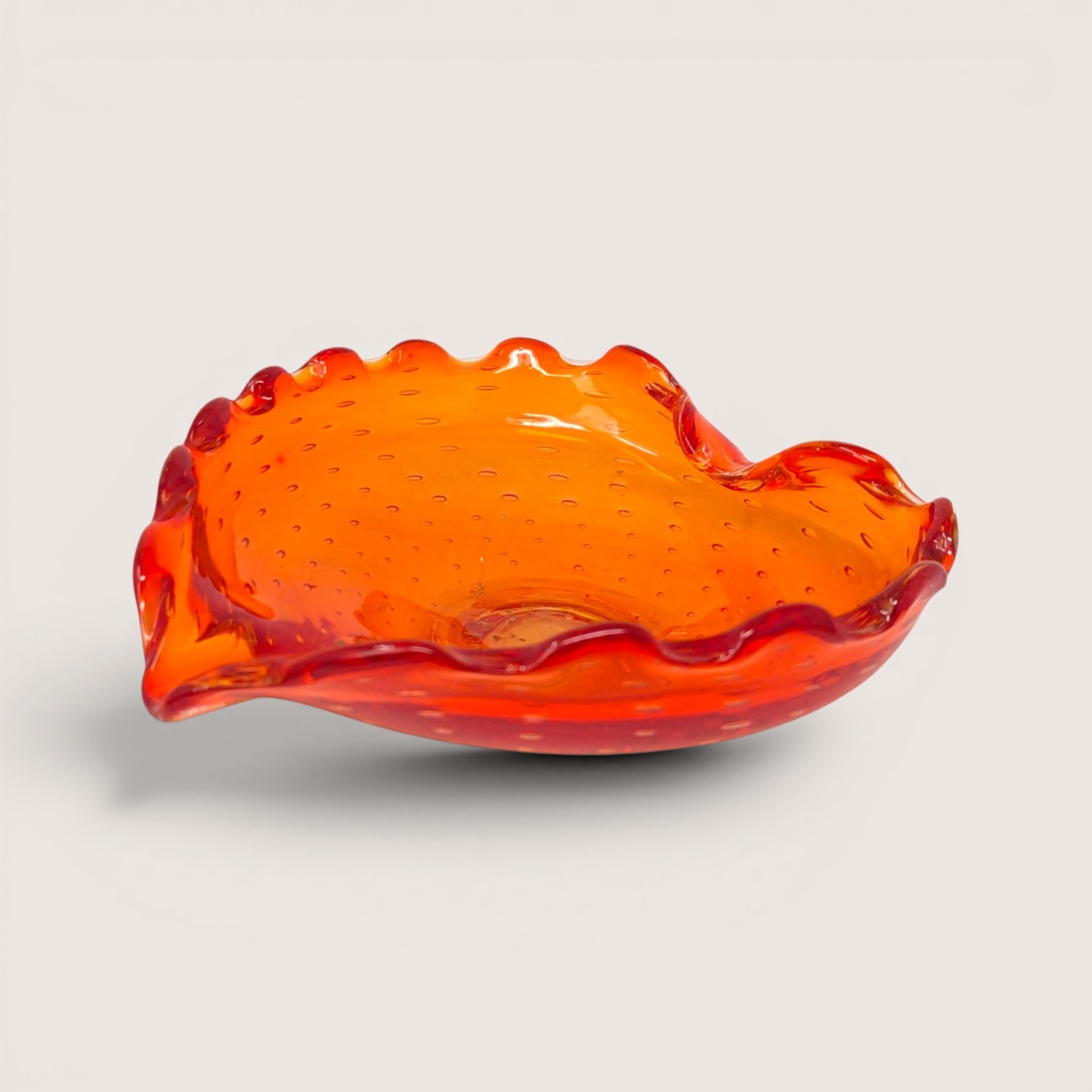 Crimson and orange Murano glass bowl featuring a controlled bubble pattern and ruffled edges on a solid background.