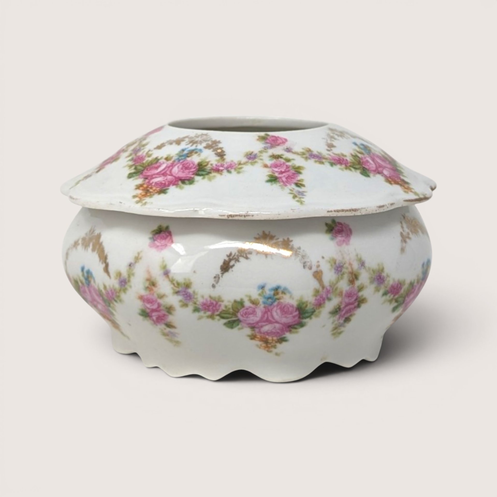An antique porcelain hair receiver with pink floral swags and gold trim on a plain white background