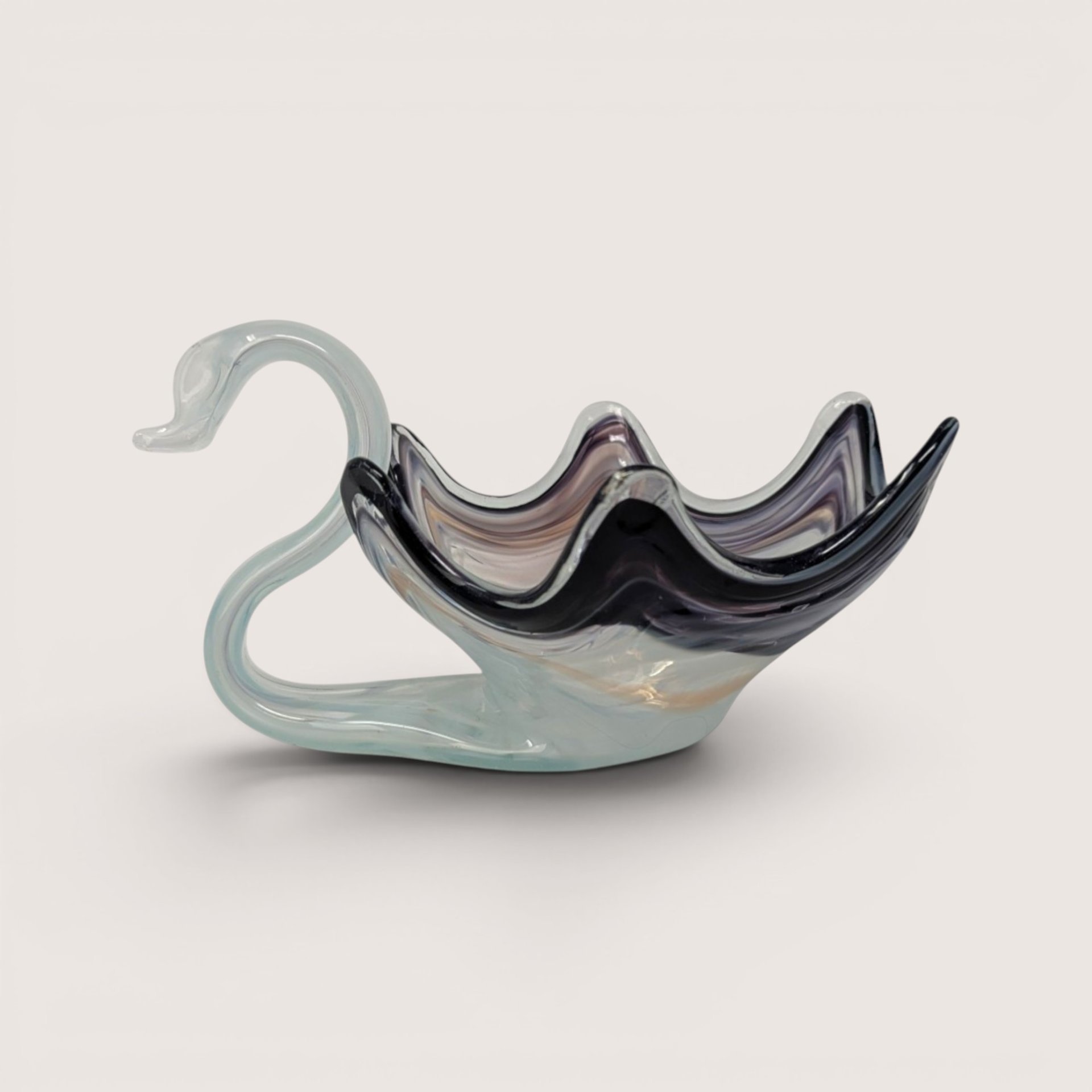 A hand blown art glass swan bowl with a light blue neck and ruffled dark purple and white body on a plain white background