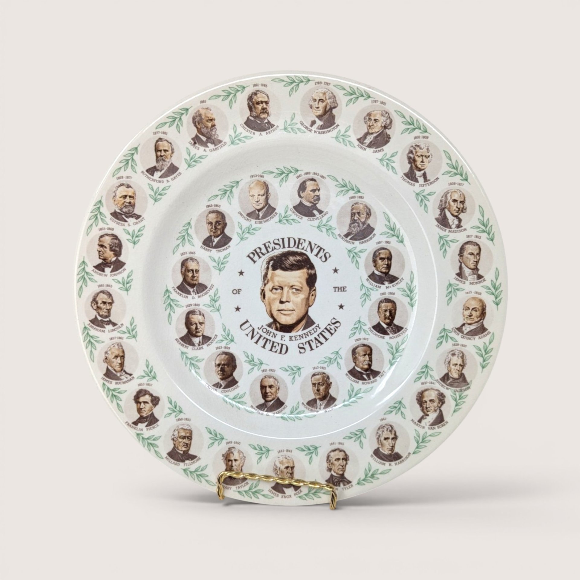 A round ceramic souvenir plate featuring portraits of US presidents with John F Kennedy at the center on a white background