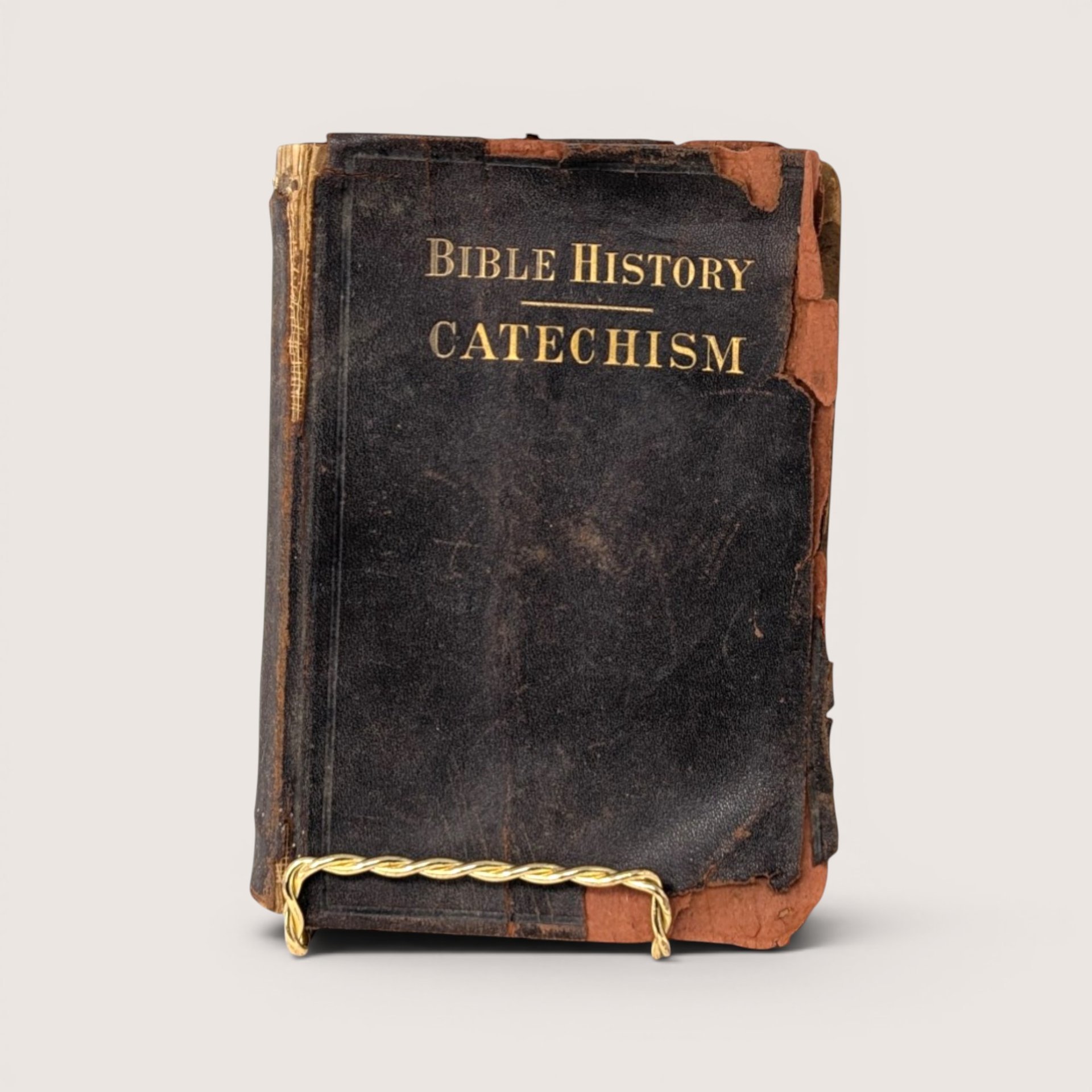 An antique Bible History Catechism book with a heavily worn black cover and gold lettering on a plain background