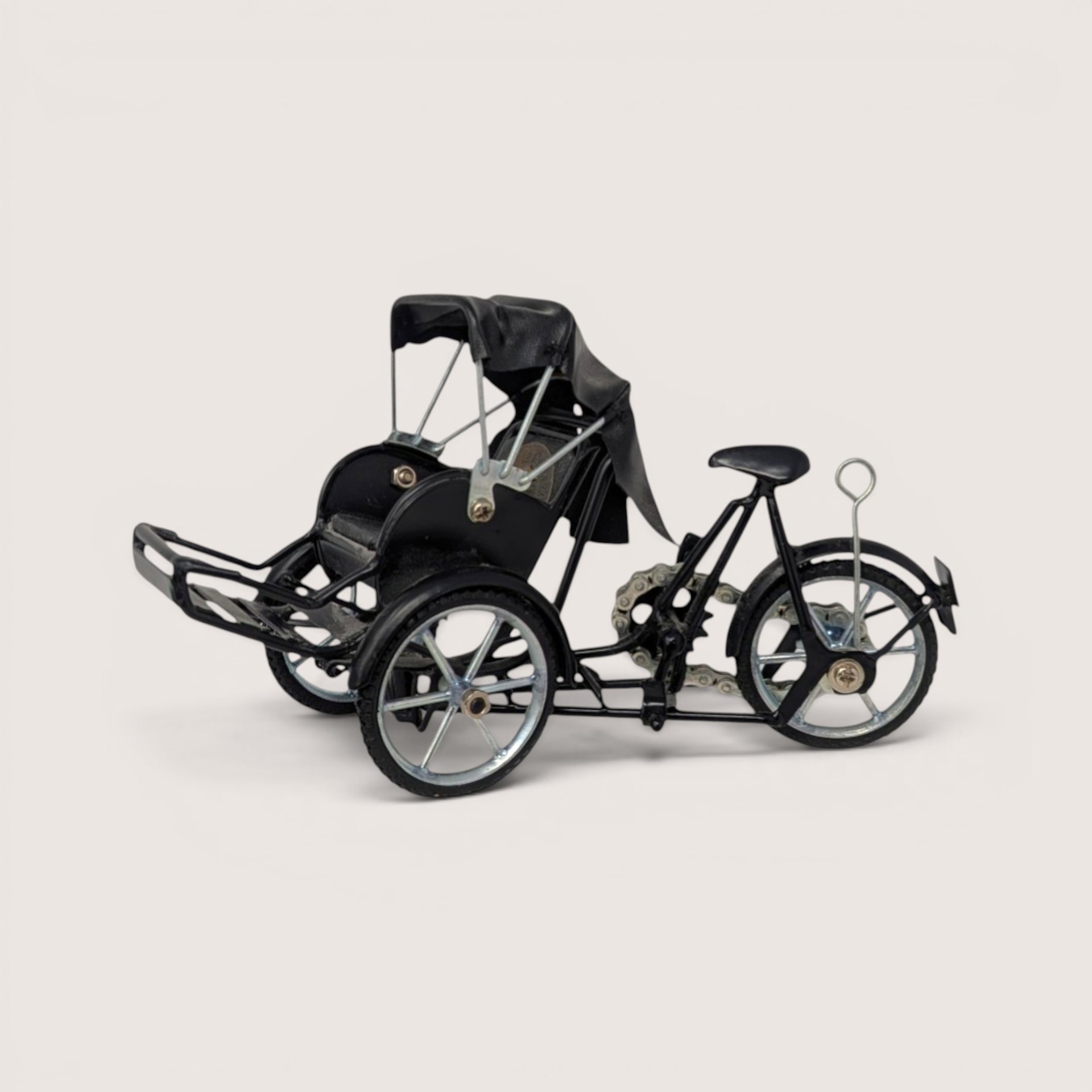 A miniature black metal model of a traditional Vietnamese cyclo rickshaw with silver wheels on a plain background