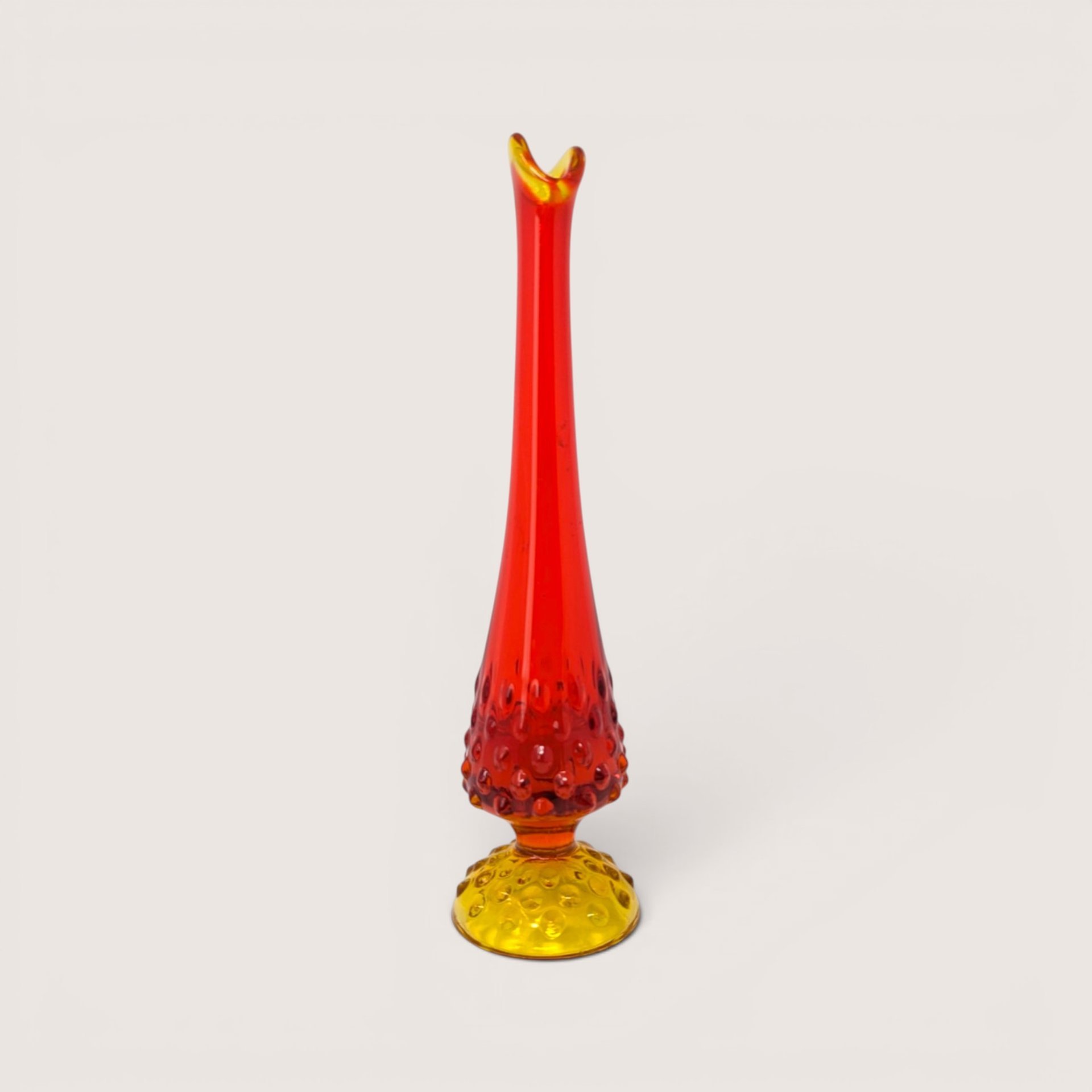 A vintage swung glass vase with a hobnail texture transitioning from a yellow base to a vibrant red pulled neck.