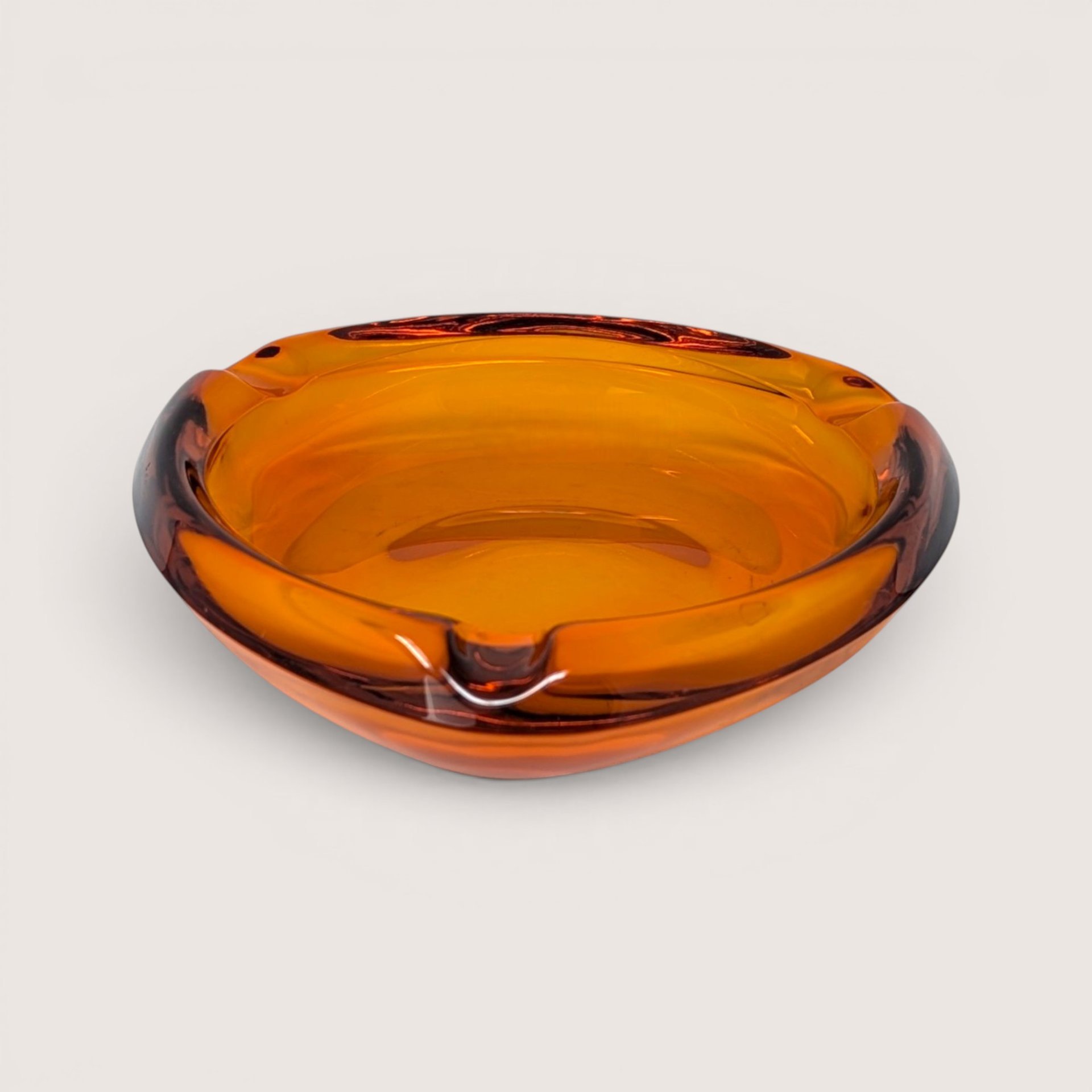 A heavy vintage amber glass ashtray with an organic asymmetrical shape and multiple rests on a plain background