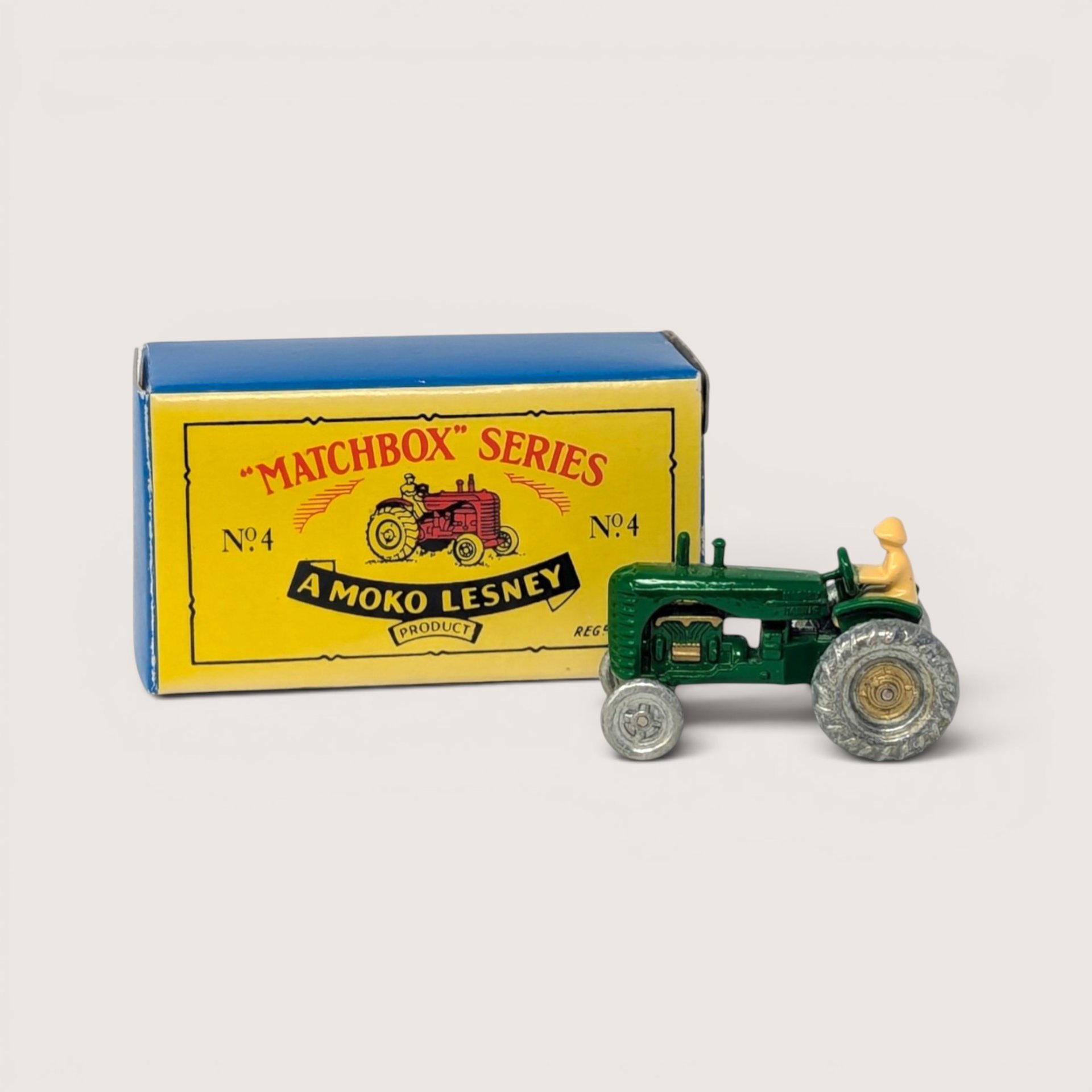 A tiny vintage green diecast tractor with a driver figure next to its original yellow and blue Matchbox Series box