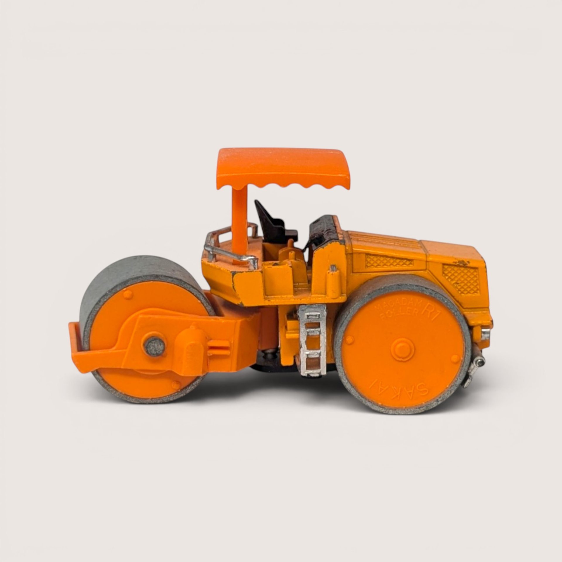 A vintage orange diecast construction toy steam roller with grey metal rollers against a plain background