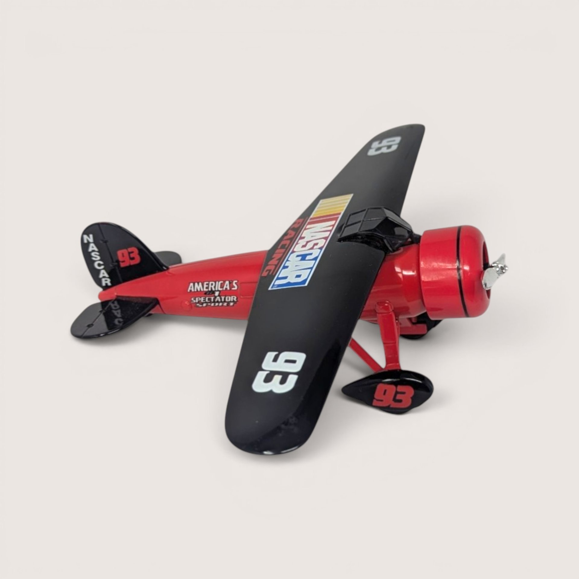 A red and black Racing Champions 1929 Travel Air Model R NASCAR die-cast airplane bank on a light background
