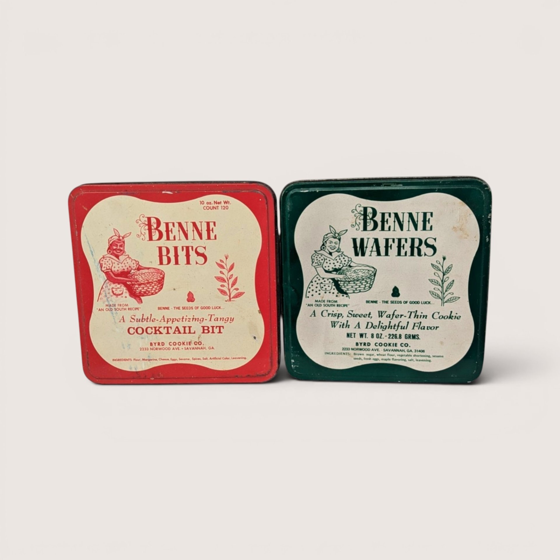 A pair of vintage square cookie tins from Byrd Cookie Co featuring red Benne Bits and green Benne Wafers on a light background