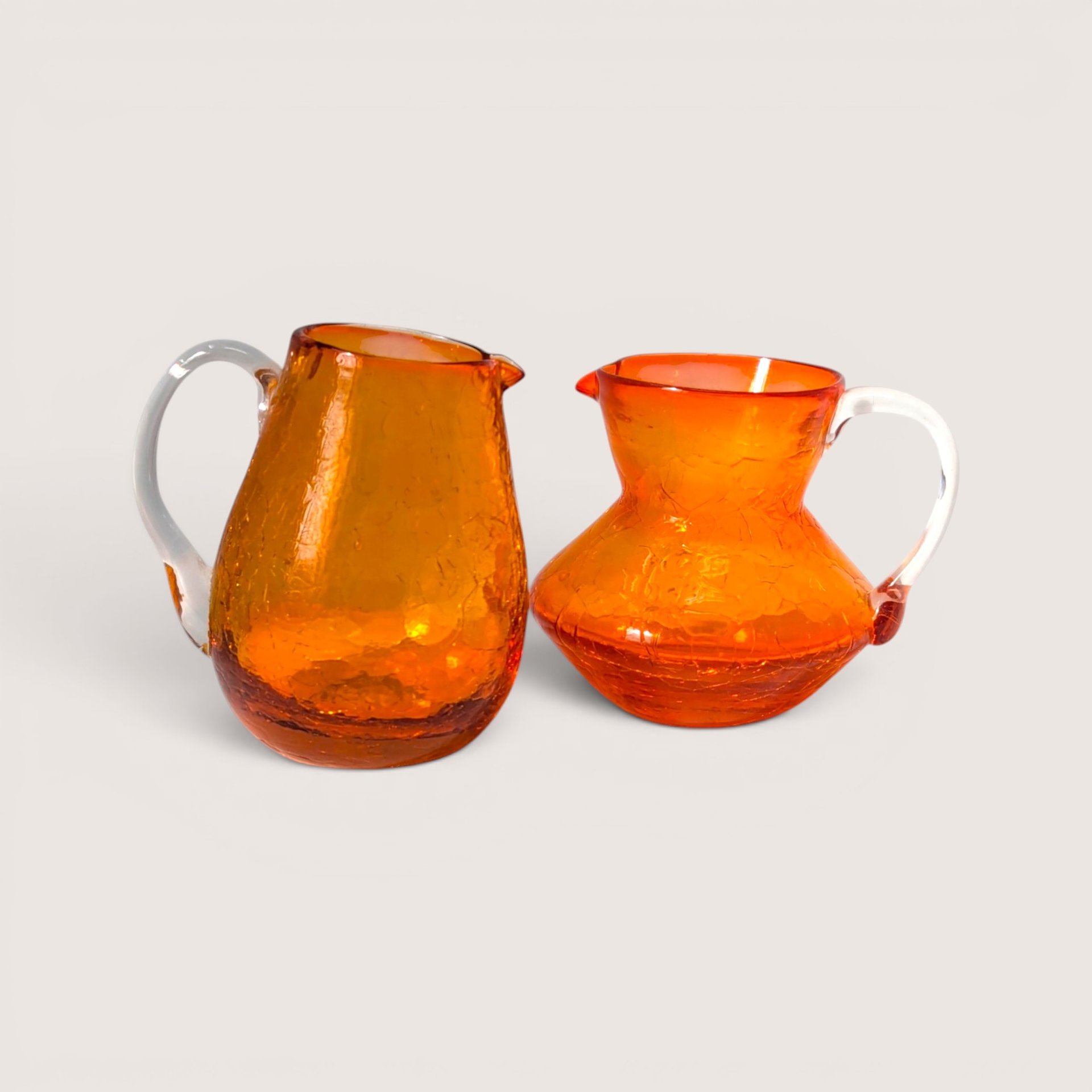 A vibrant mid-century orange crackle glass creamer and sugar bowl set with clear glass handles