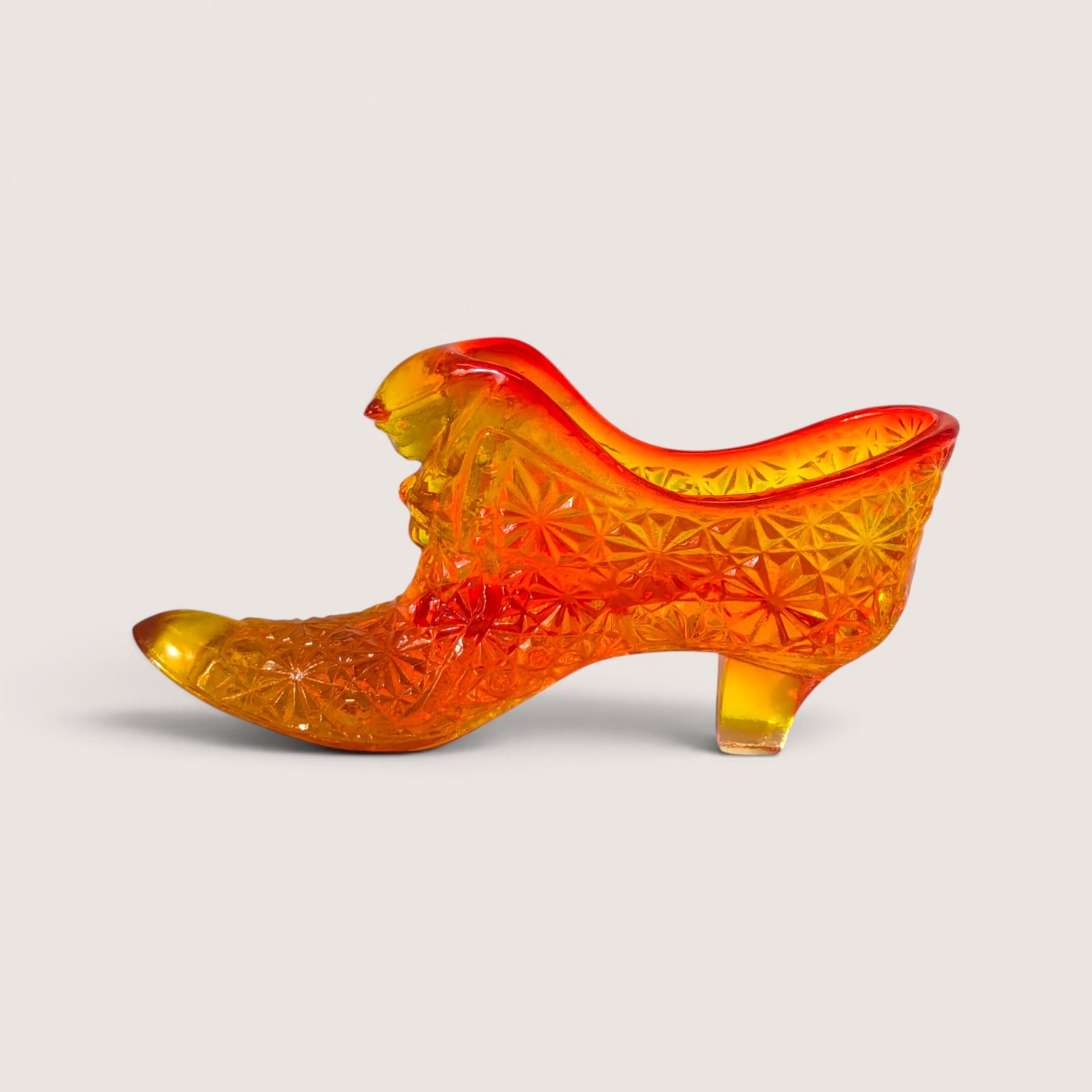 An amberina glass slipper figurine with a textured geometric pattern transitioning from yellow to red at the collar.