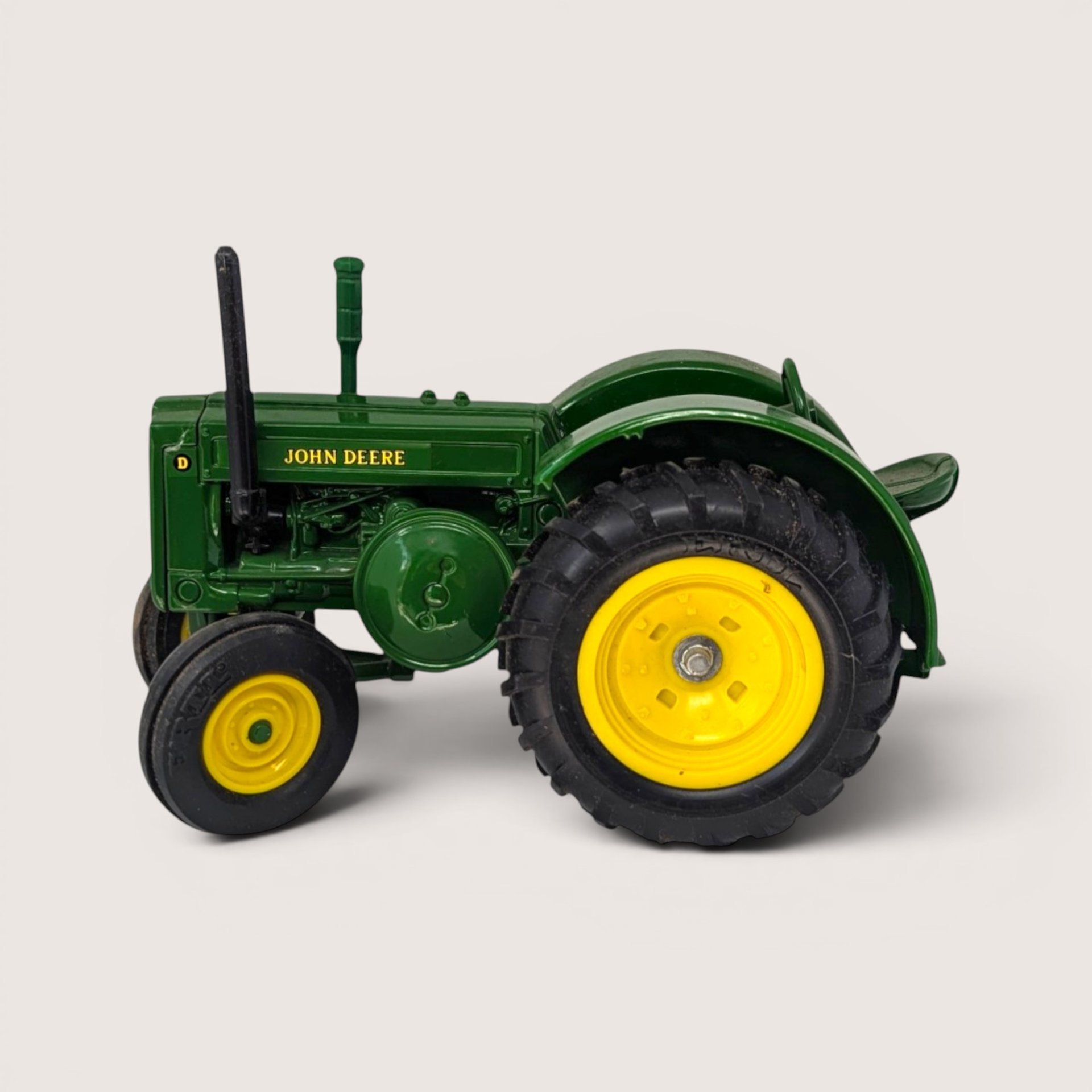 A vintage green diecast John Deere toy tractor with bright yellow wheels shown from a side profile view.