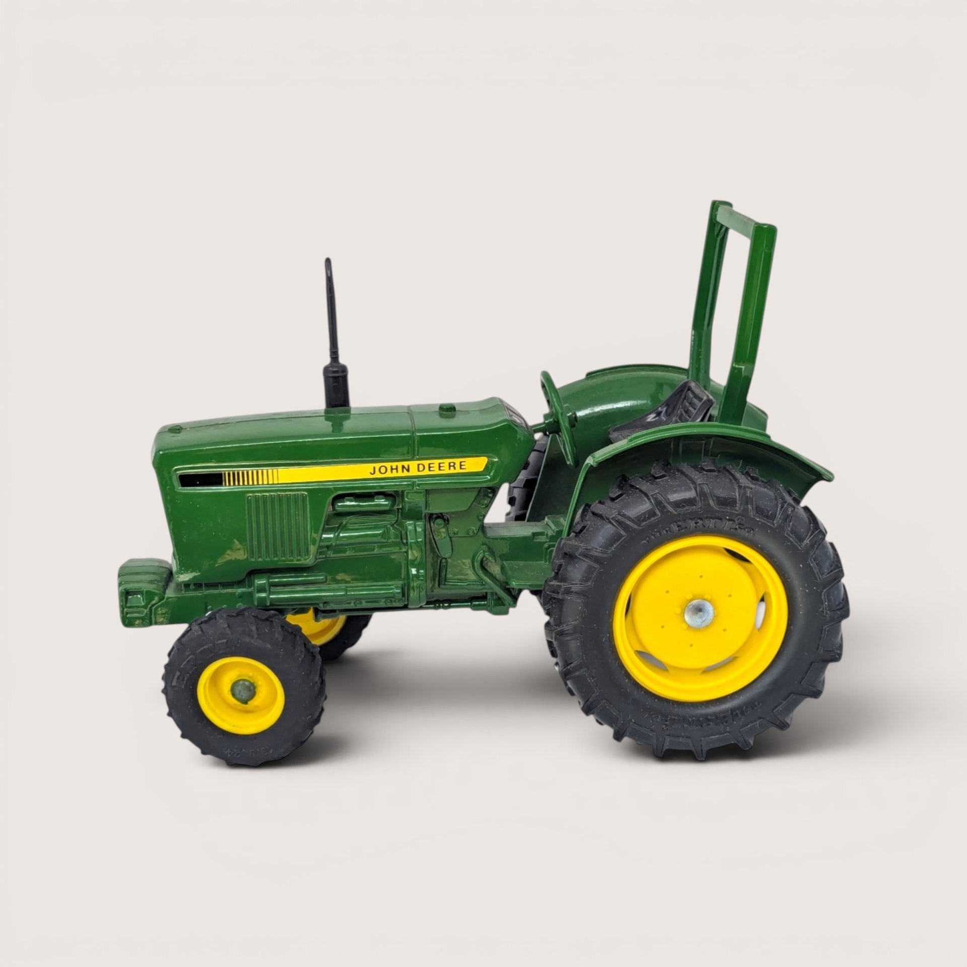 A vintage green diecast John Deere utility tractor featuring bright yellow wheels and a rear green roll guard frame.