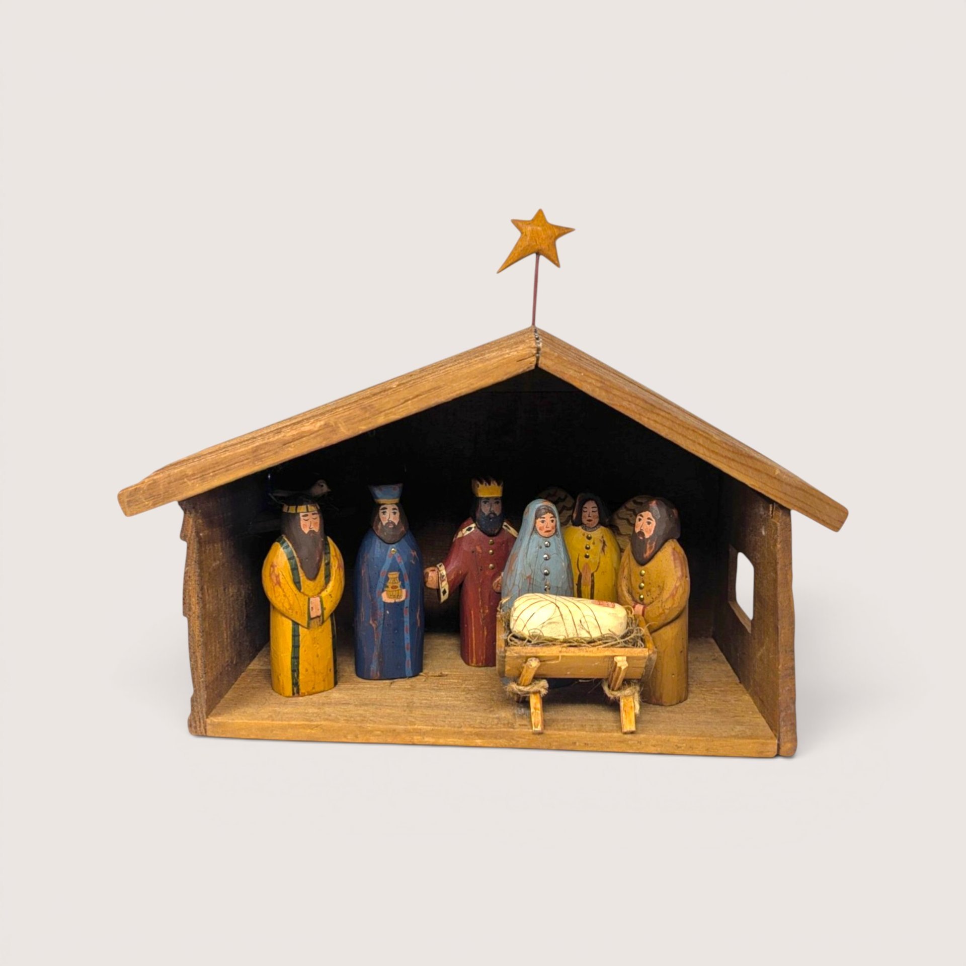 Handmade wooden creche with painted folk art nativity figures including Mary, Joseph, Wise Men, and an angel.