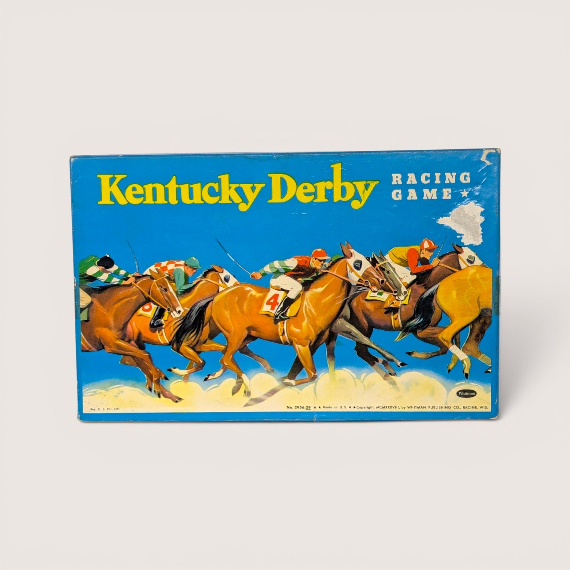 Vintage Kentucky Derby board game box featuring a vibrant illustration of jockeys racing horses on a blue background.