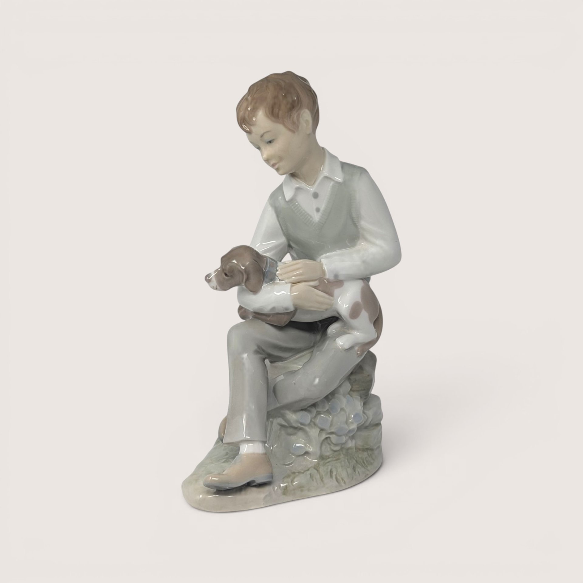 Vintage Zaphir glossy porcelain figurine of a seated boy in a vest gently holding a brown and white puppy.