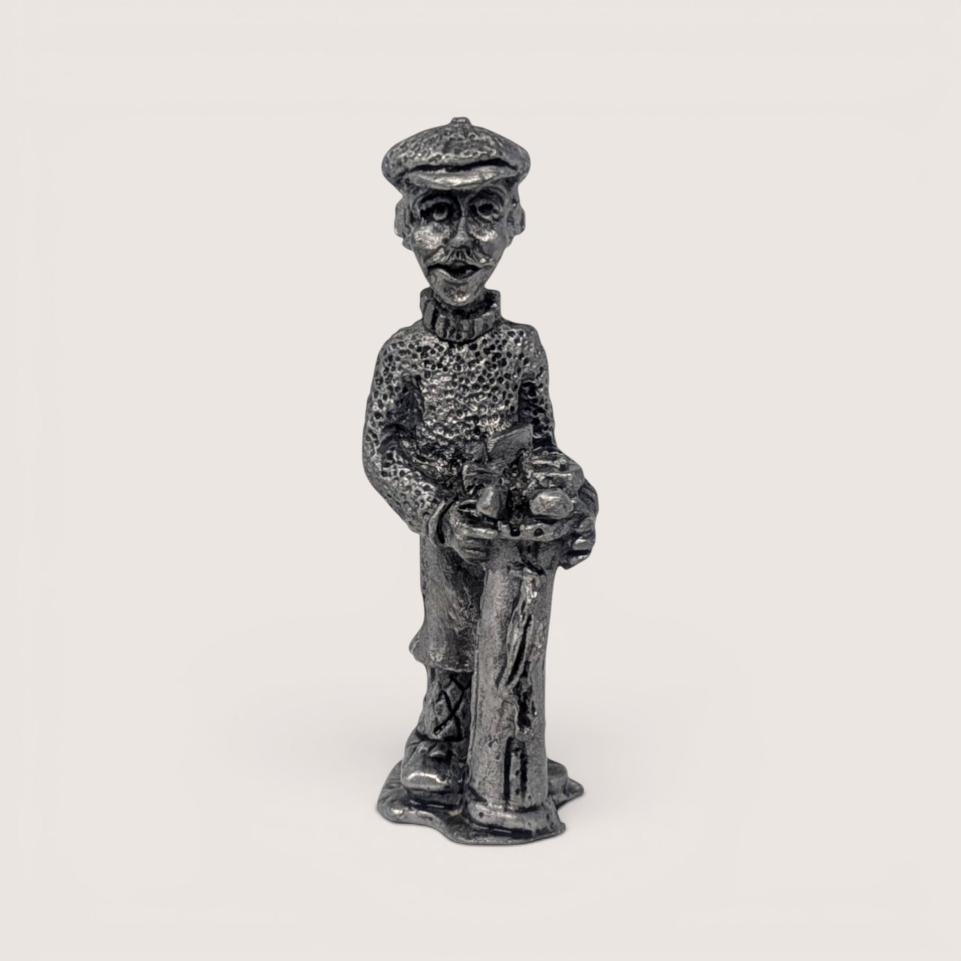 Miniature vintage pewter figurine of a male golfer wearing a flat cap and sweater leaning on his golf bag.