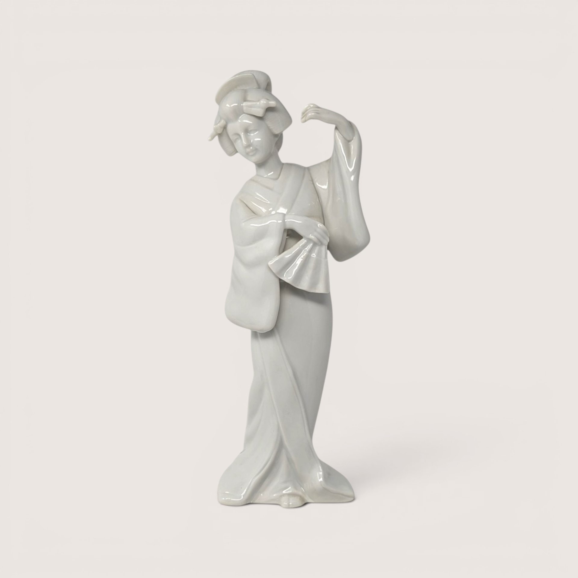 Vintage white porcelain Geisha figurine holding a fan in a traditional pose.
