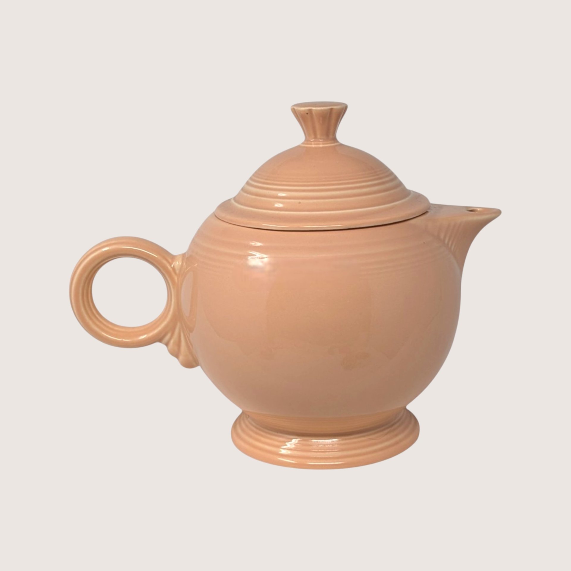 Vintage Fiesta peach glazed ceramic covered teapot featuring signature concentric rings and matching lid.