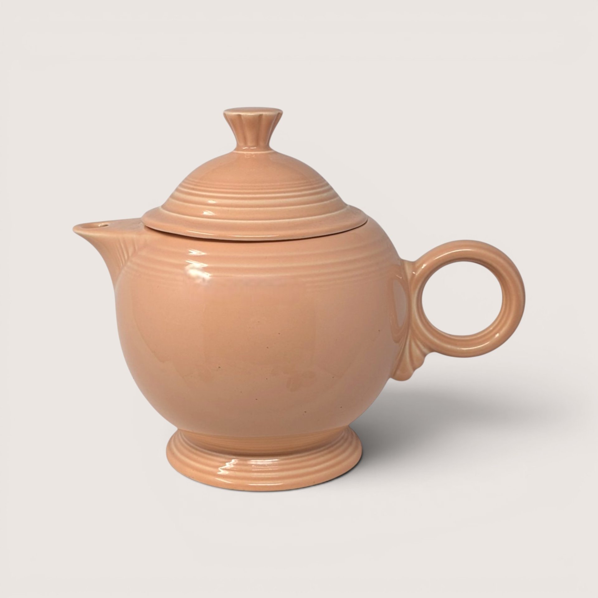 Vintage Fiesta peach glazed ceramic covered teapot featuring signature concentric rings and matching lid.