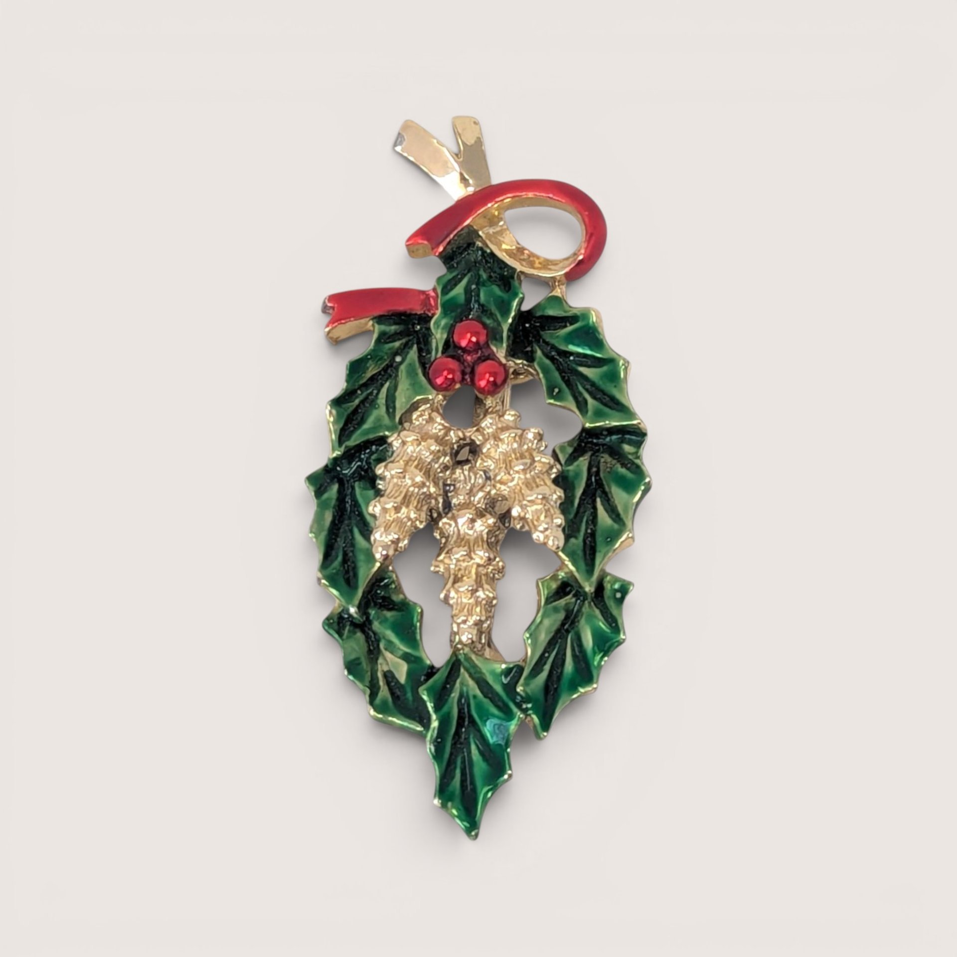 Vintage gold tone and enamel Christmas brooch featuring green holly leaves, red berries, and a red ribbon bow.