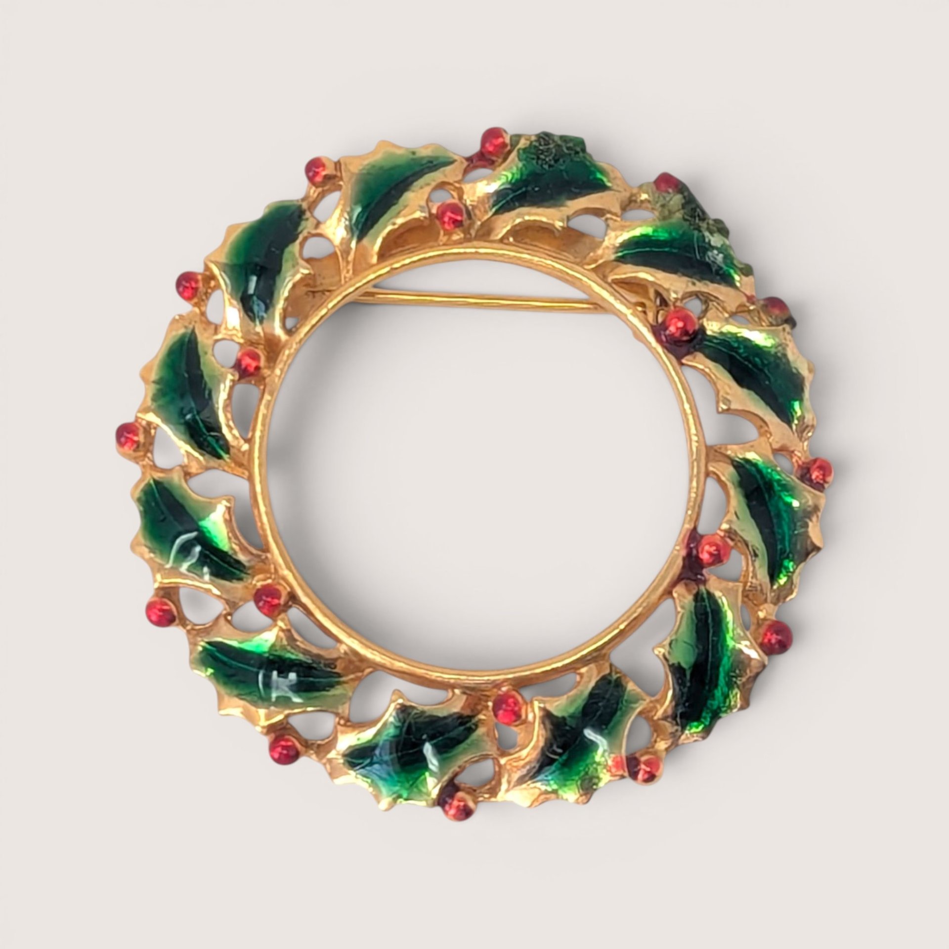 Vintage gold-tone enamel holly wreath brooch with green leaves and red berry details.