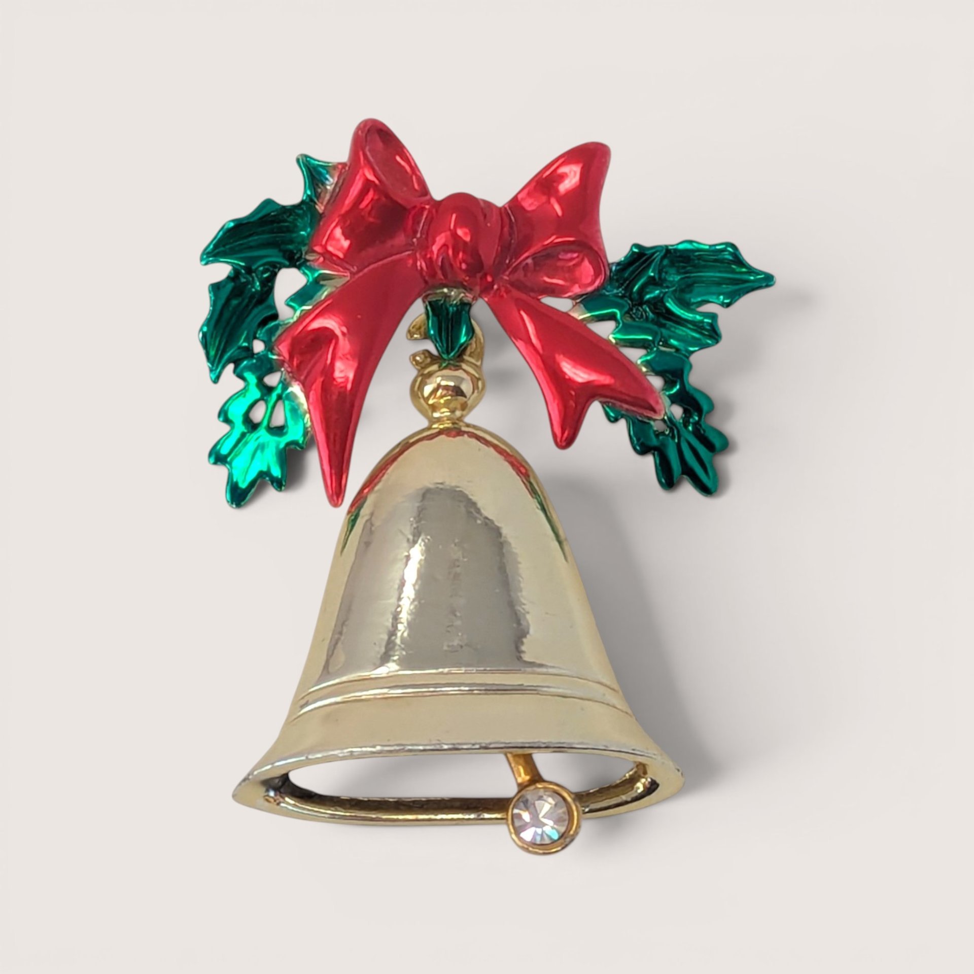 Vintage gold-tone Christmas bell brooch with red enamel bow, green holly leaves, and a rhinestone clapper.