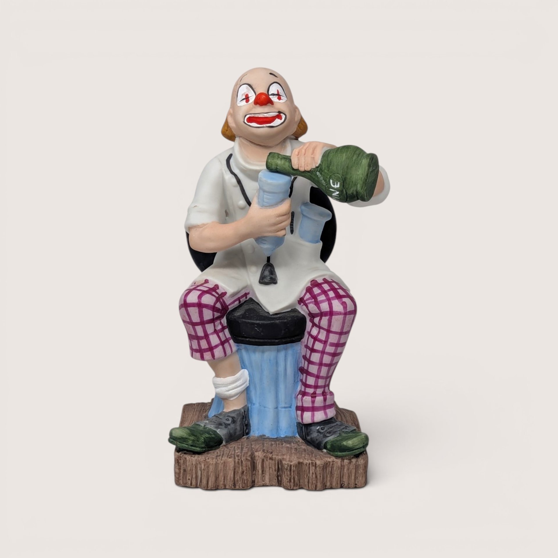 Vintage Toscany ceramic clown figurine sitting on a chair and pouring wine from a bottle into a glass.