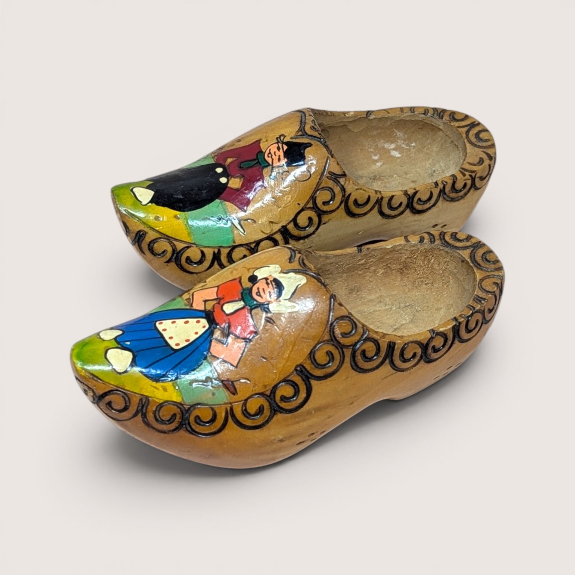 Pair of vintage hand-painted Dutch wooden clogs featuring traditional figures and carved swirl borders.