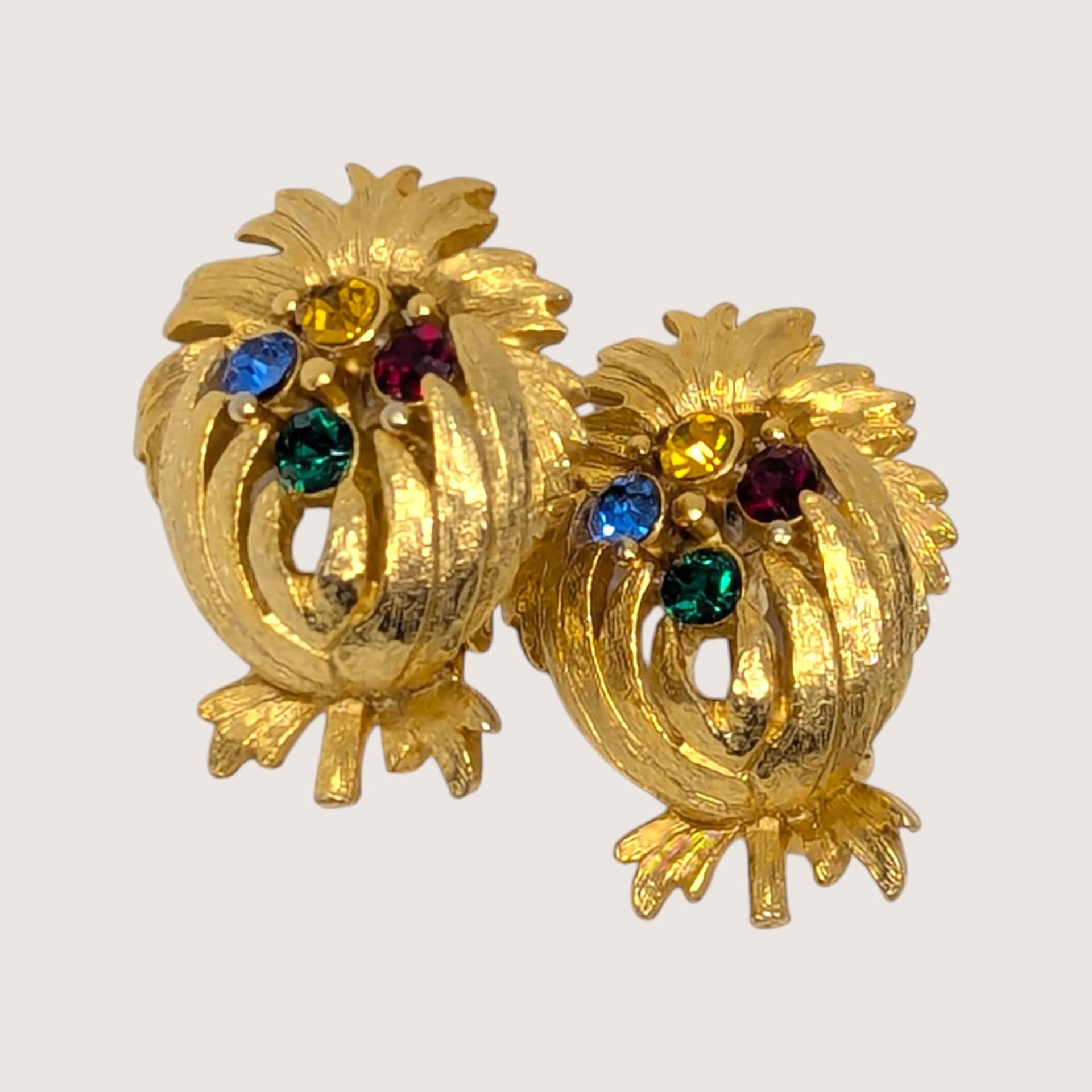 A pair of vintage gold-tone textured clip-on earrings shaped like pineapples and inset with multi-colored rhinestones against a neutral background.