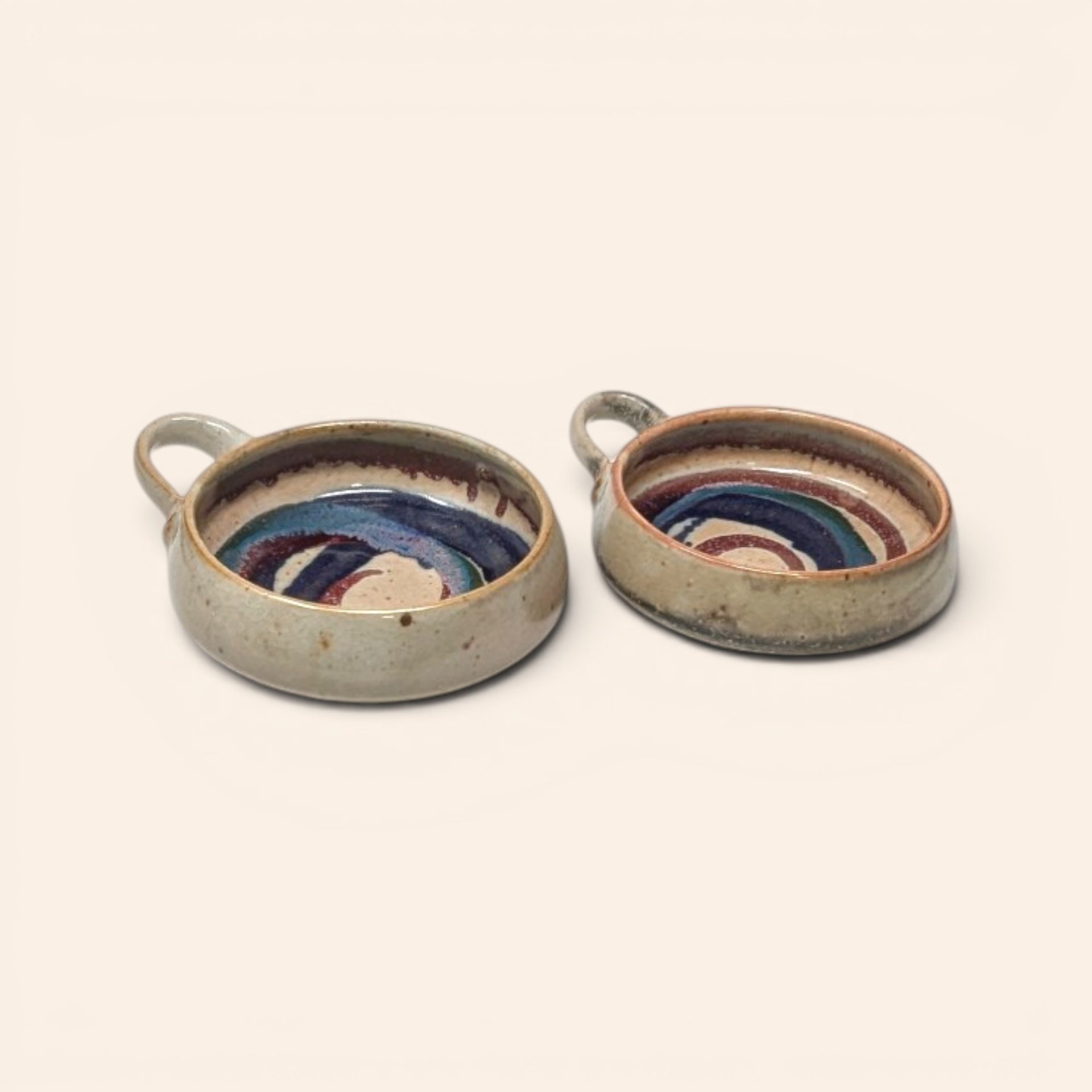Set of two handmade stoneware bowls with handles and interior multi-colored glaze swirl patterns.