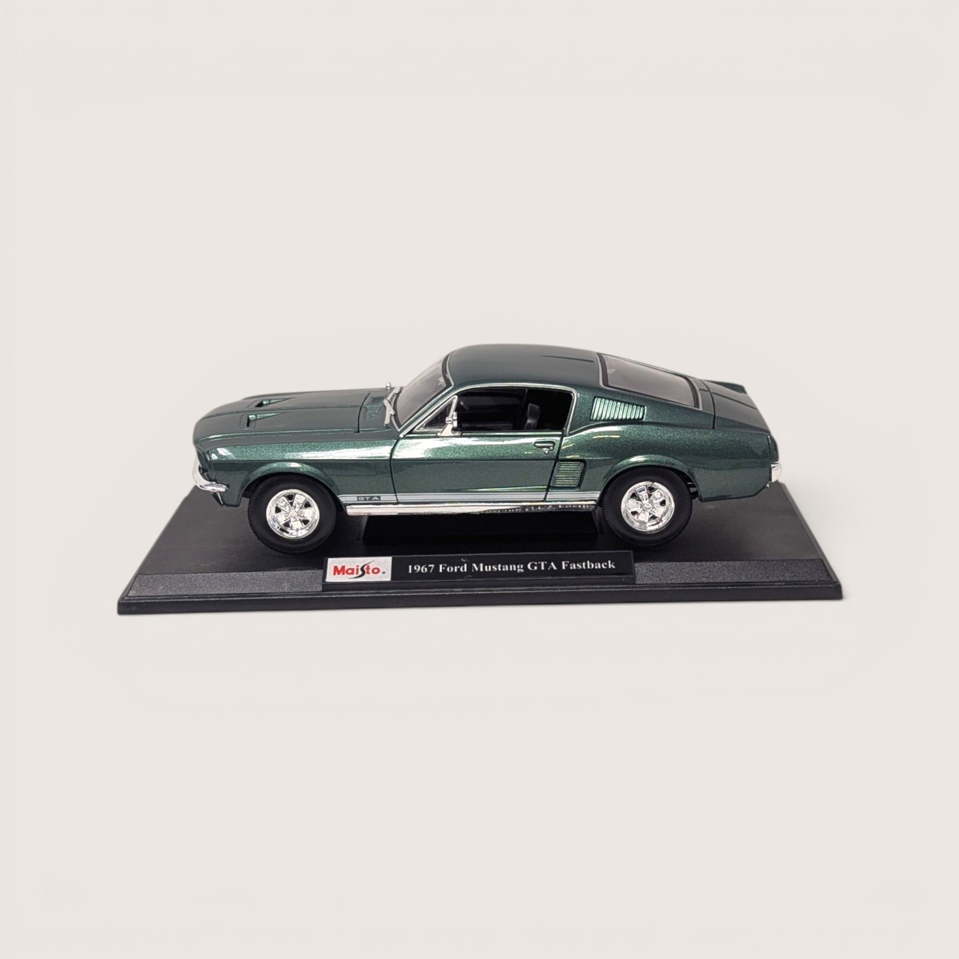 Vintage Maisto dark metallic green 1967 Ford Mustang GTA Fastback die-cast vehicle in its original window box set against a plain linen background.