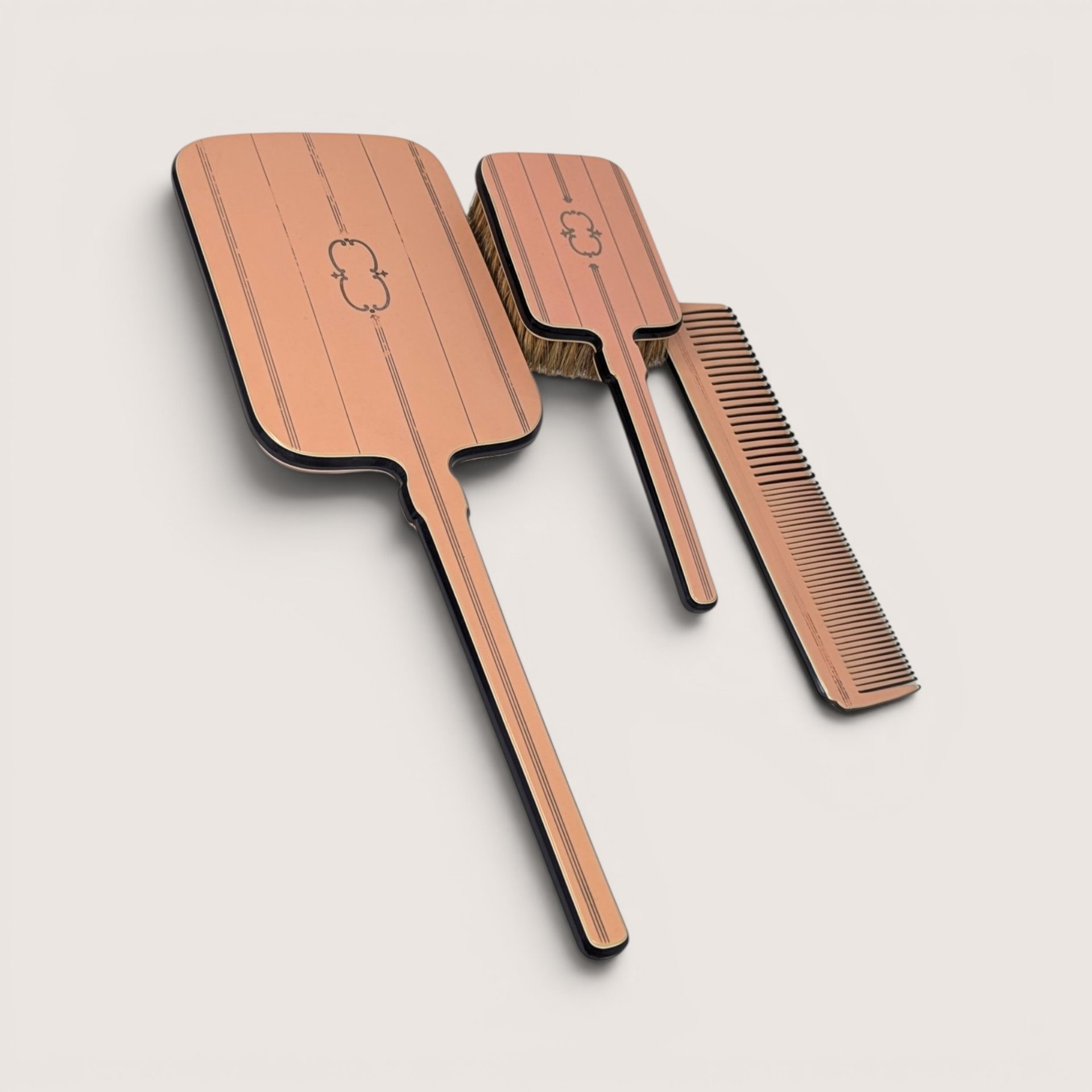 Vintage pink and black vanity hand mirror, hair brush, and comb set set against a plain linen background.