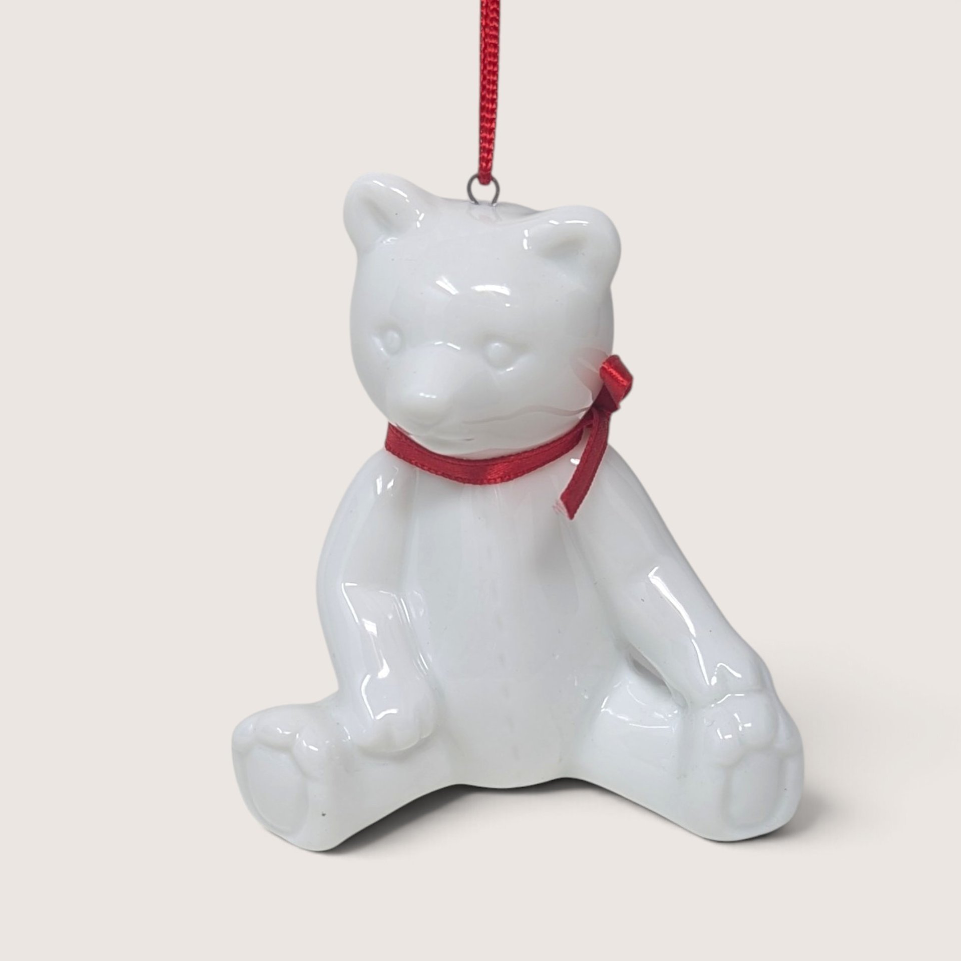 Vintage Dept 56 glossy white porcelain sitting teddy bear Christmas tree ornament with a red ribbon.