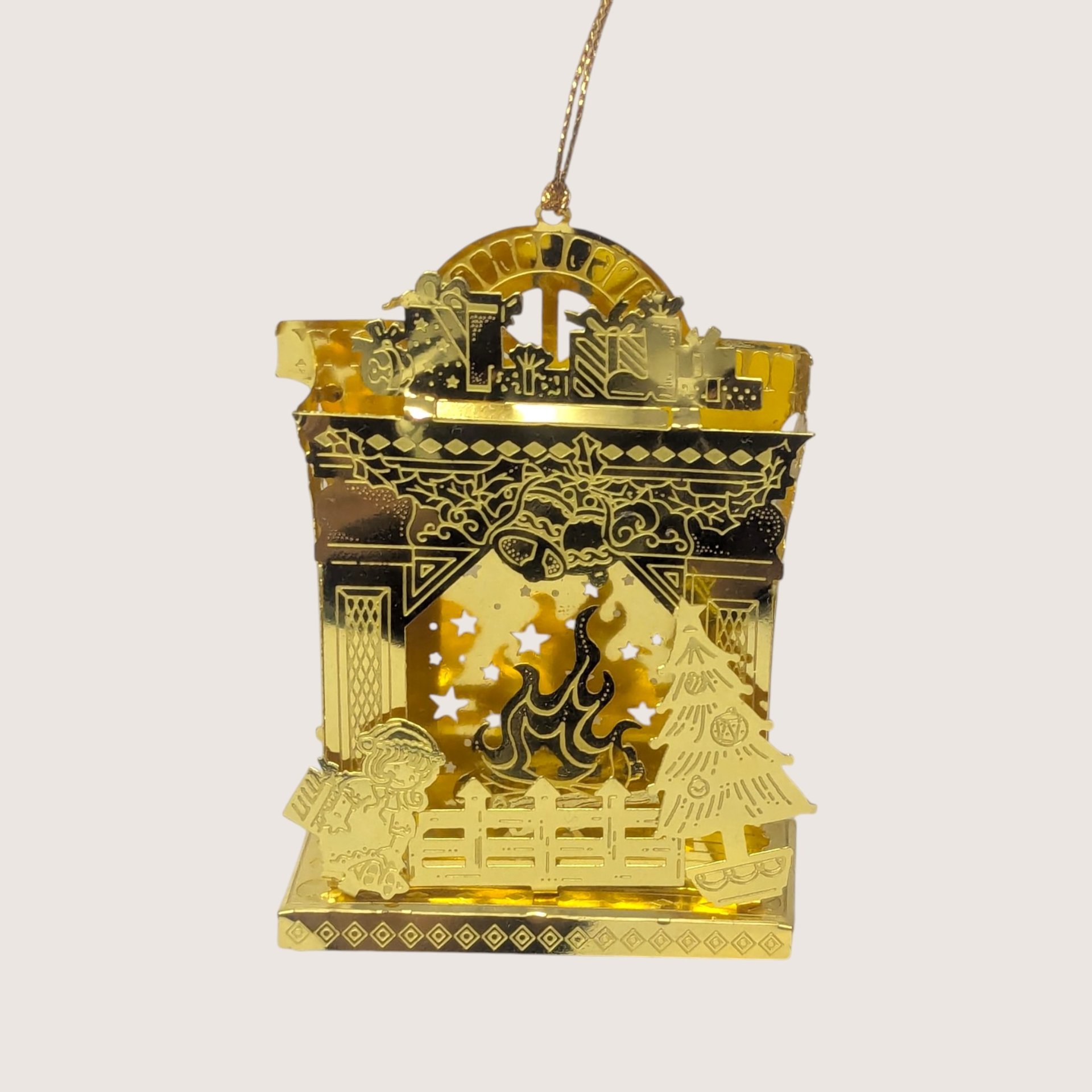 Vintage gold-tone laser-cut metal fireplace Christmas ornament featuring a hearth scene, stockings, and a built-in socket for a tree light.