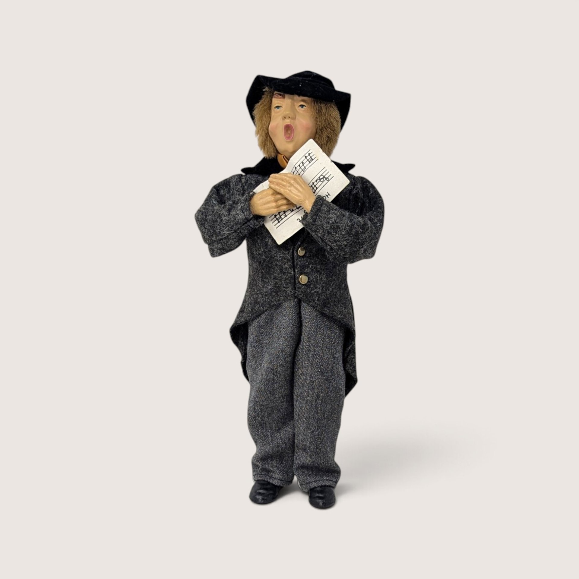 Vintage molded plastic Christmas caroler figurine wearing a grey coat and holding sheet music.