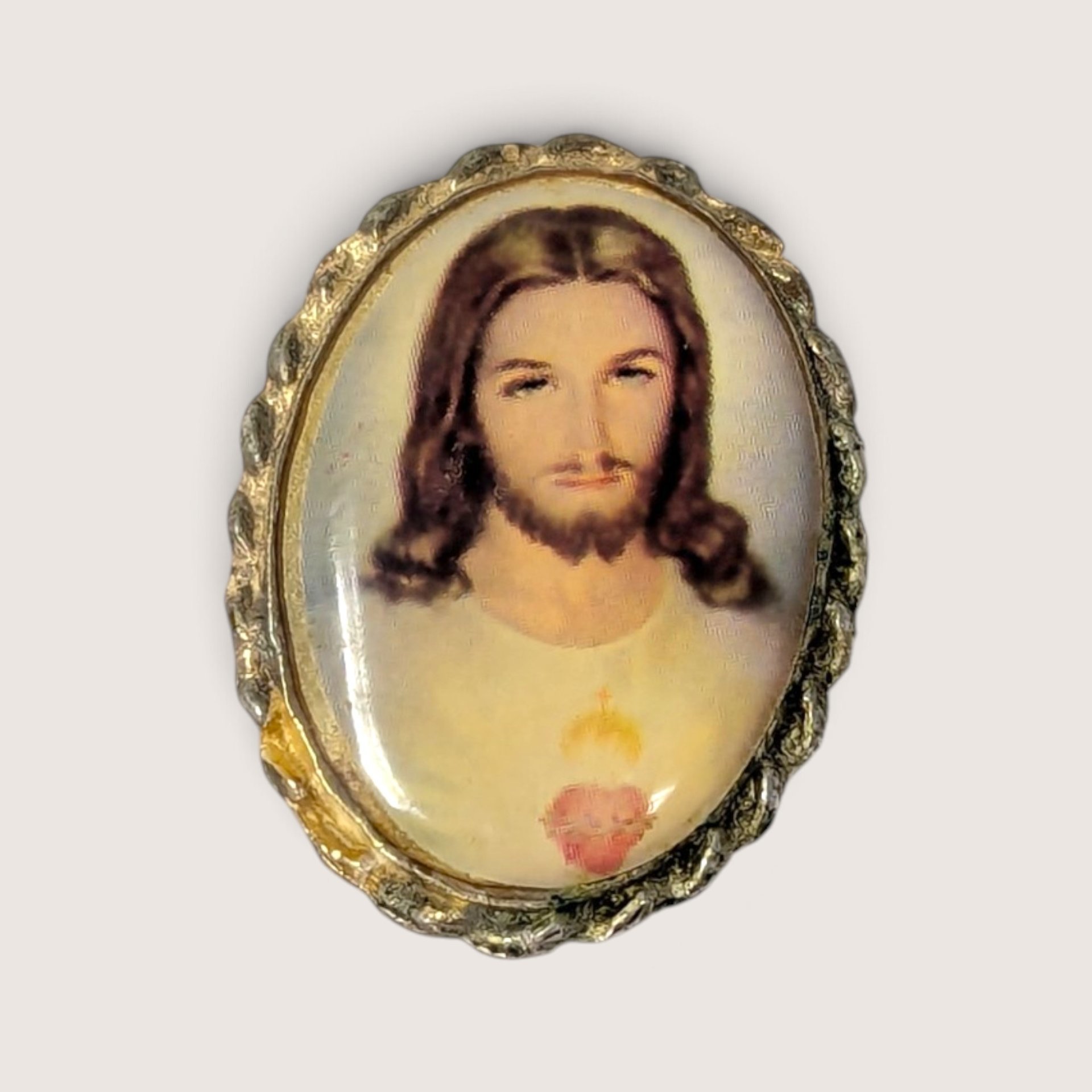 Vintage religious brooch featuring a portrait of the Sacred Heart of Jesus in a decorative scalloped metal frame.