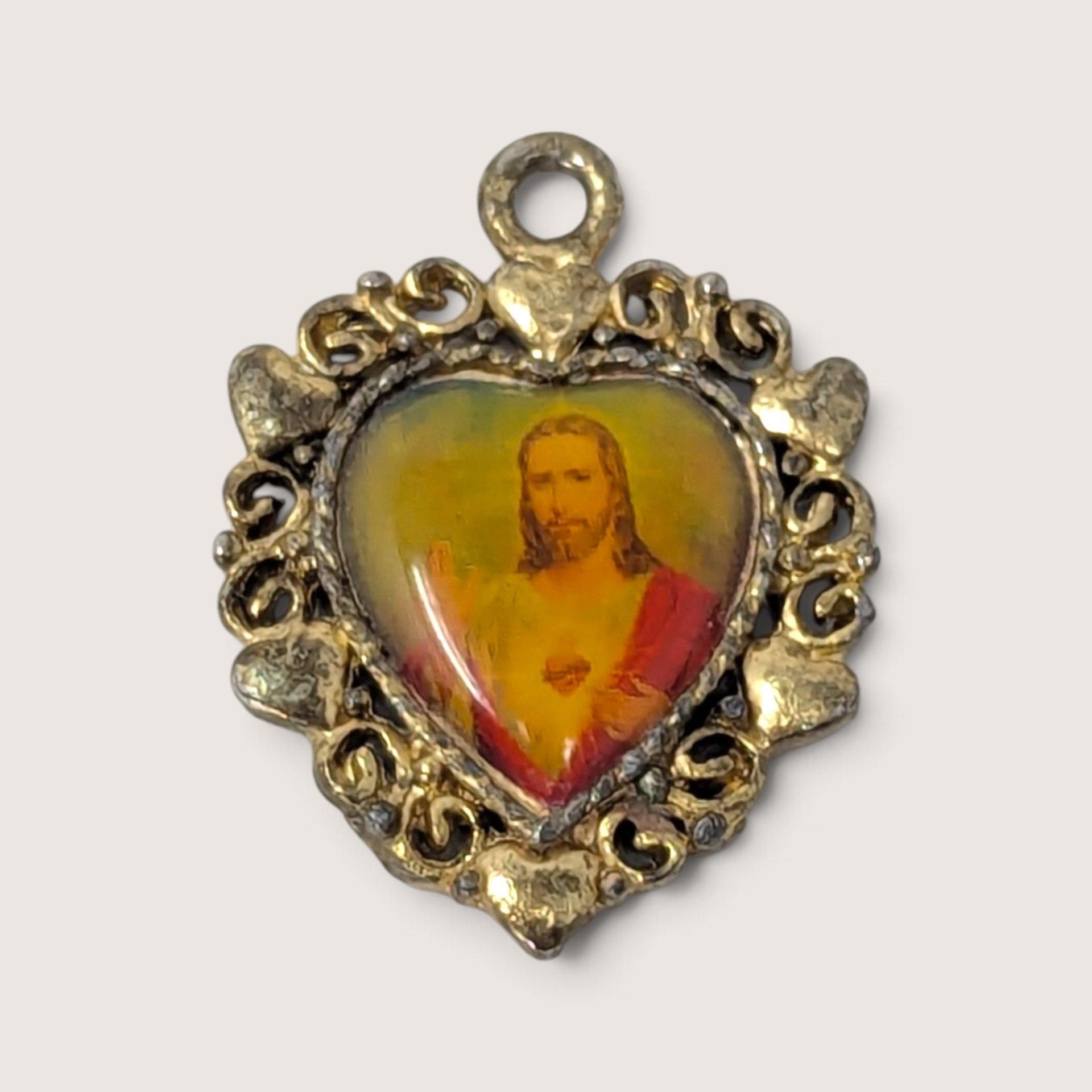Vintage religious pendant featuring a portrait of the Sacred Heart of Jesus in an ornate heart-shaped metal frame.