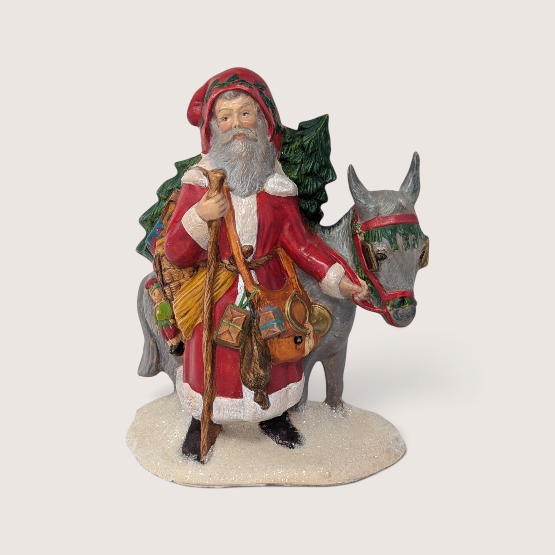 Vintage hand-painted ceramic old world Santa figurine standing with a mule and a Christmas tree on a snowy base.