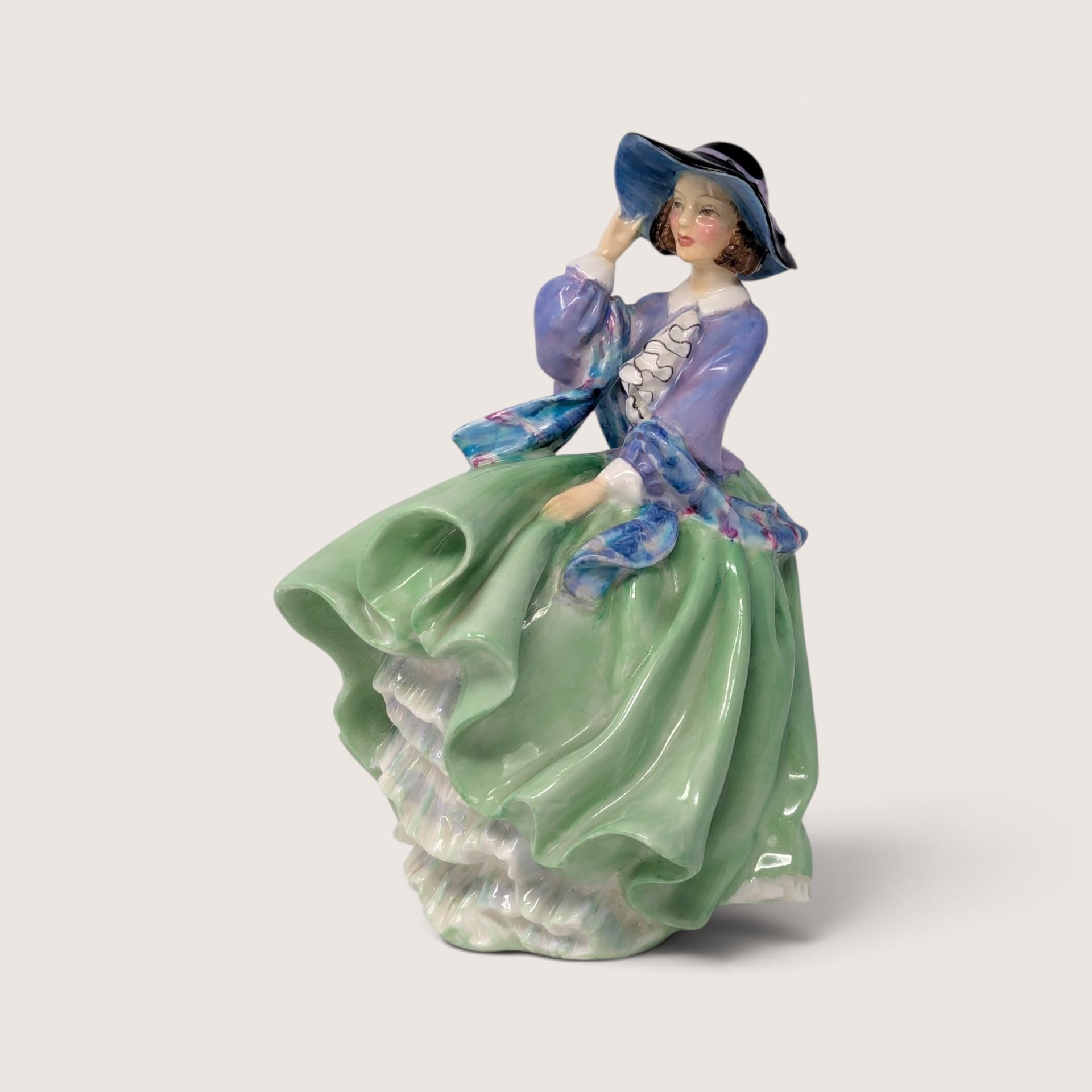 Vintage Royal Doulton porcelain Top O the Hill figurine depicting a lady in a green skirt and blue bodice adjusting her hat.