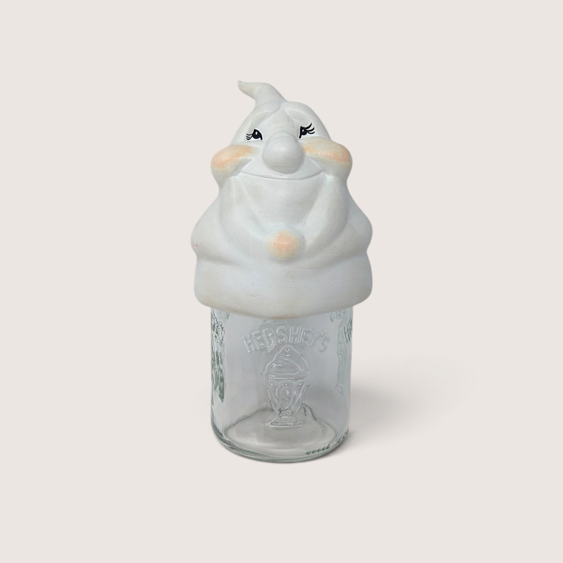 Vintage ceramic ghost mason jar topper with painted rosy cheeks sitting on a clear Hershey glass jar.