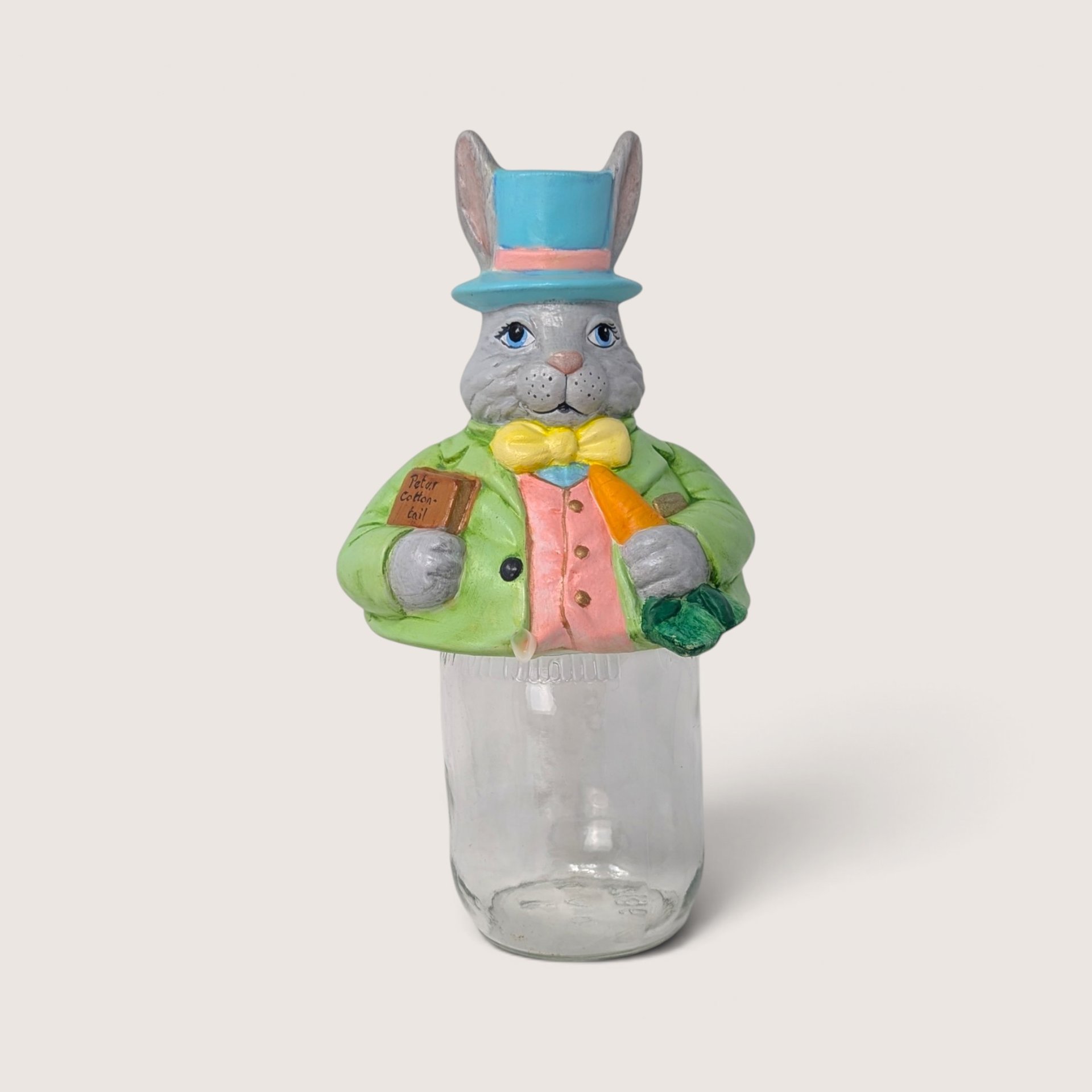 Vintage ceramic Easter bunny mason jar topper wearing a blue top hat sitting on a clear glass jar.
