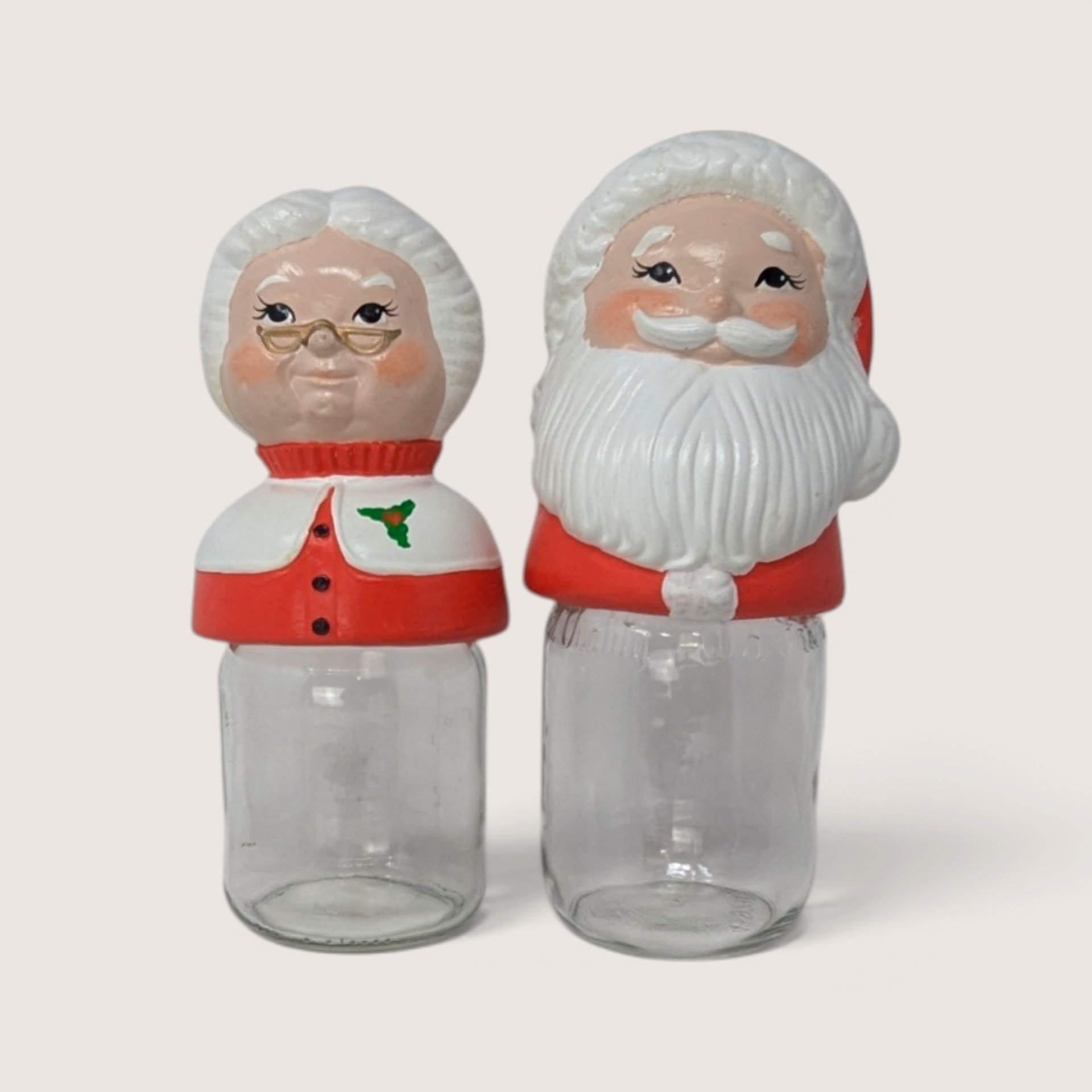 Vintage ceramic Mr and Mrs Claus mason jar toppers sitting on clear glass jars.