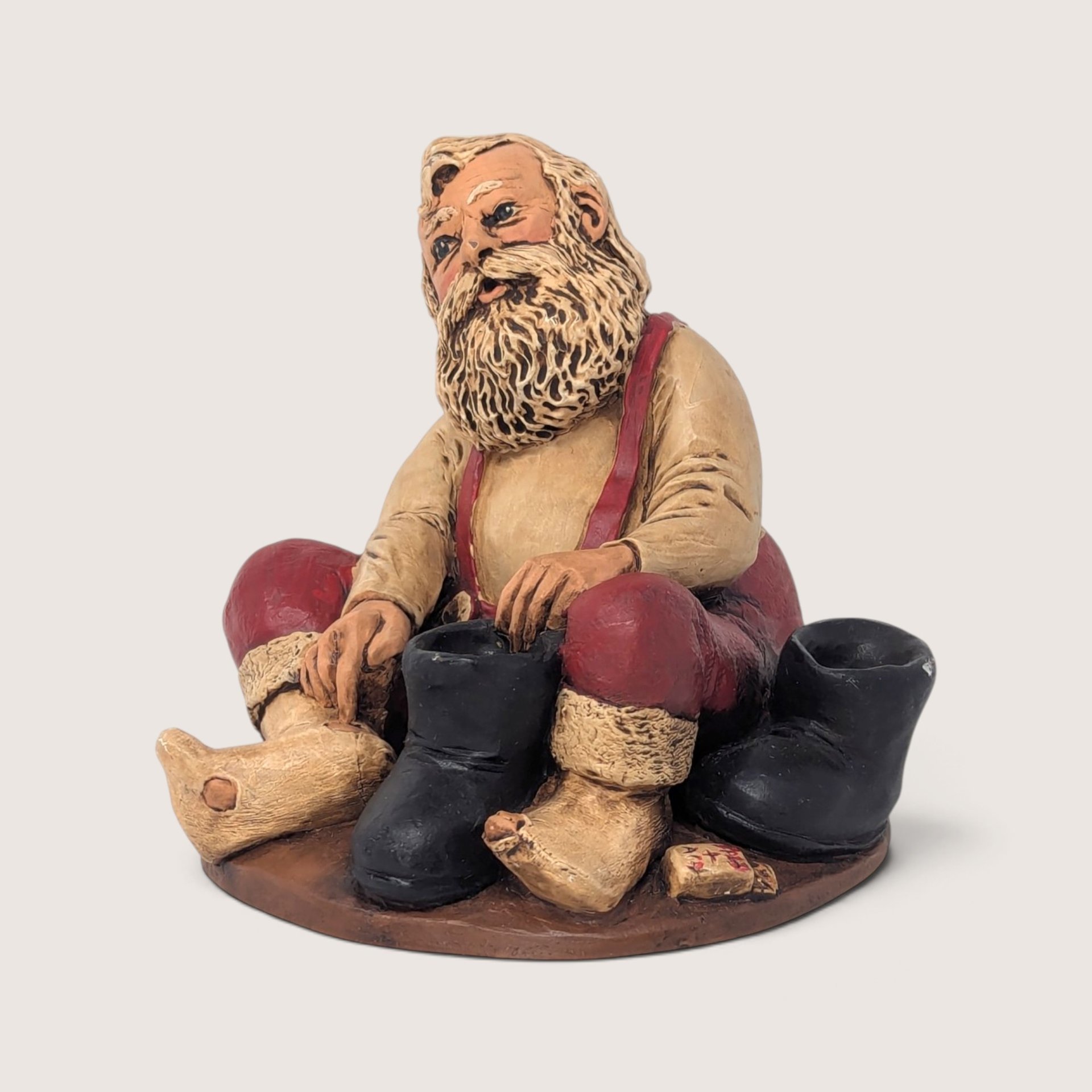 Vintage resin holiday figurine of Santa Claus sitting down and putting on his black boots.
